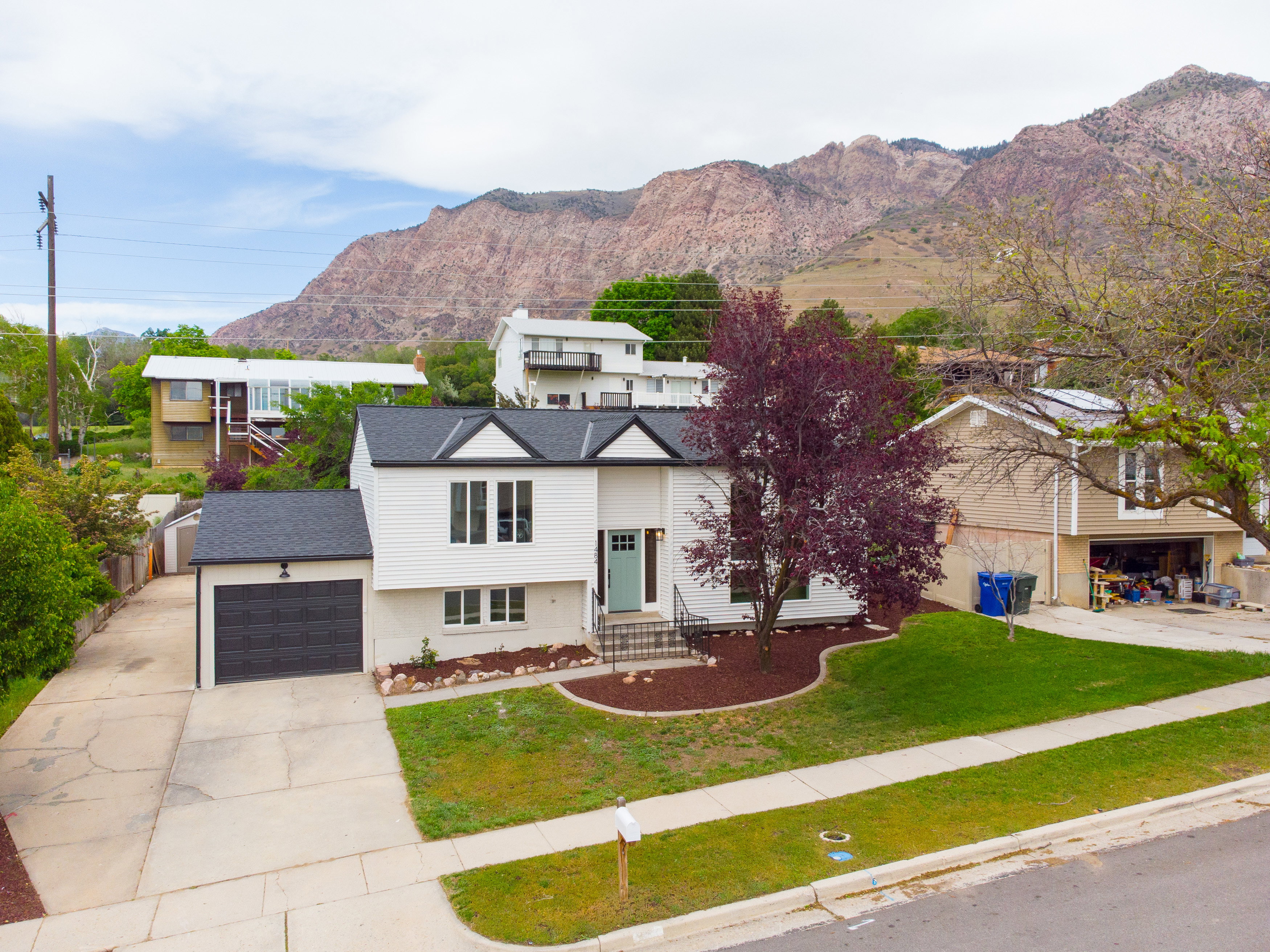 Modernized split-level residence featuring white siding, a contrasting black roof, and a turquoise front door