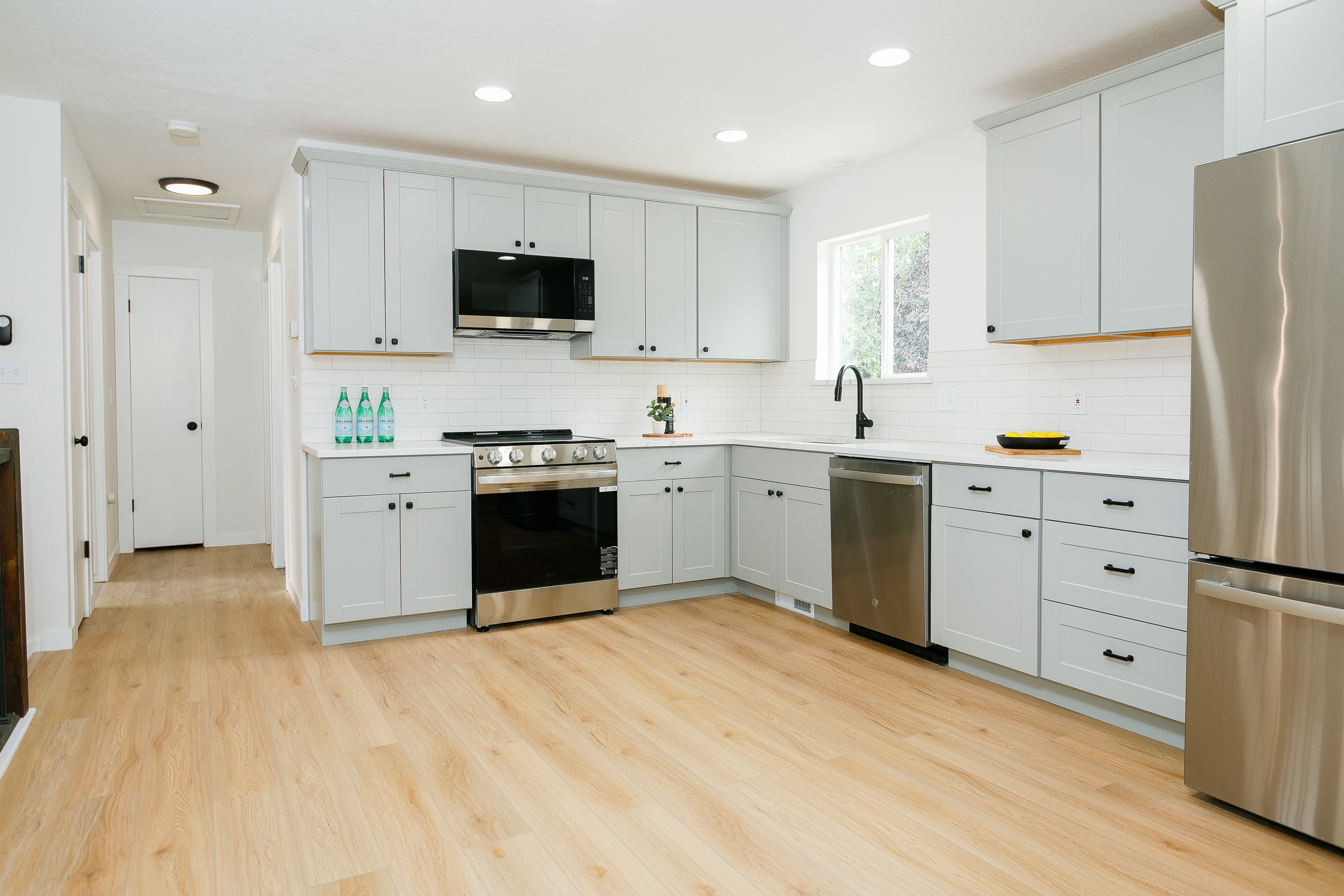 Kitchen featuring light wood-finish flooring, white subway tile backsplash, light gray cabinetry with black hardware, stainless steel appliances, and recessed lighting