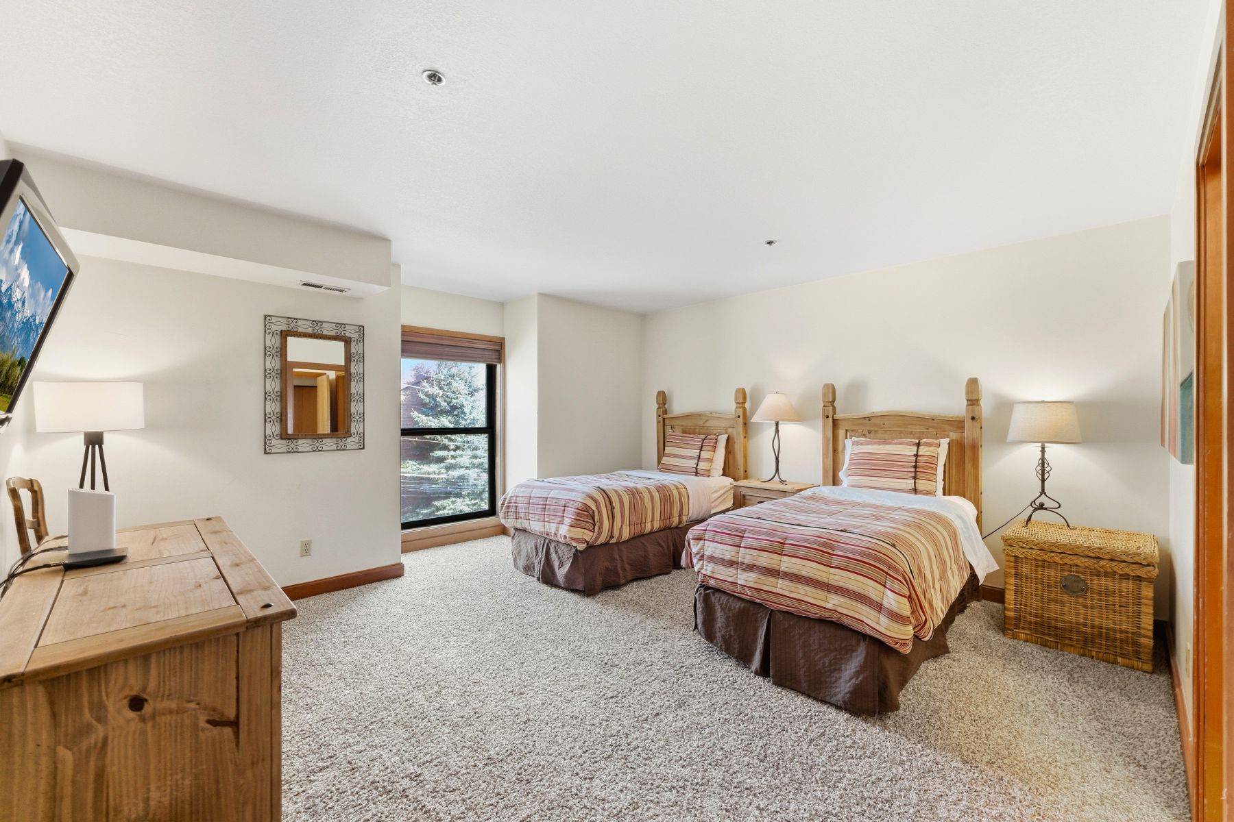 Carpeted room featuring two wood-frame beds with striped bedding, a large picture window with a wood-finish frame, and light-toned walls