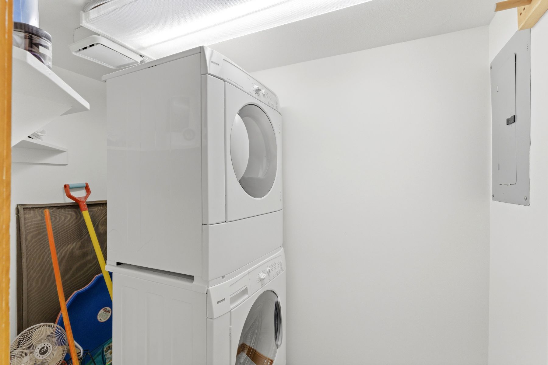 Dedicated laundry space featuring a stacked washer and dryer, ceiling-mounted lighting, and integrated wall shelving