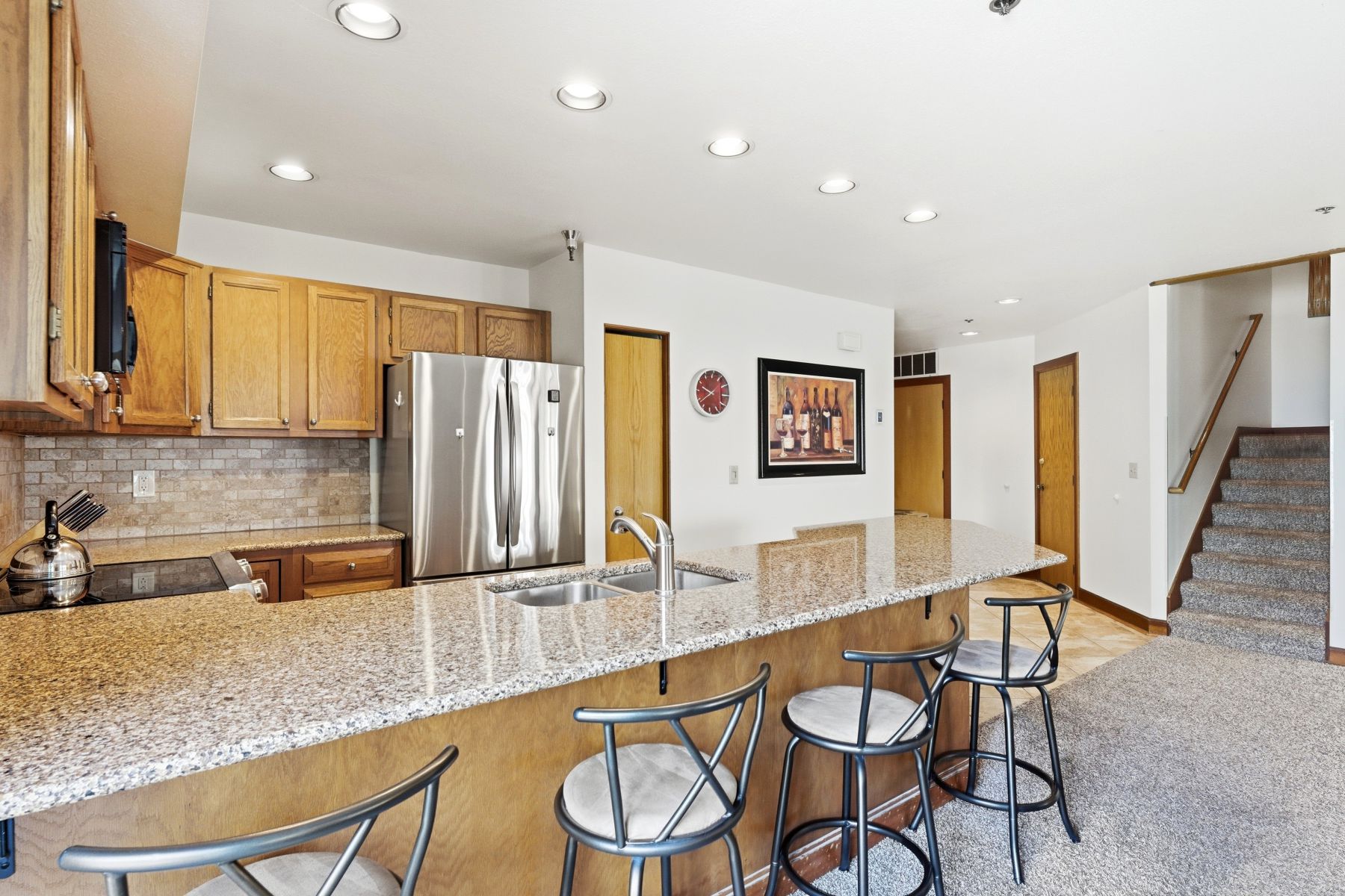 Kitchen featuring a large granite-style island with built-in stainless steel sink, wood-finish cabinetry, and stainless steel French door refrigerator