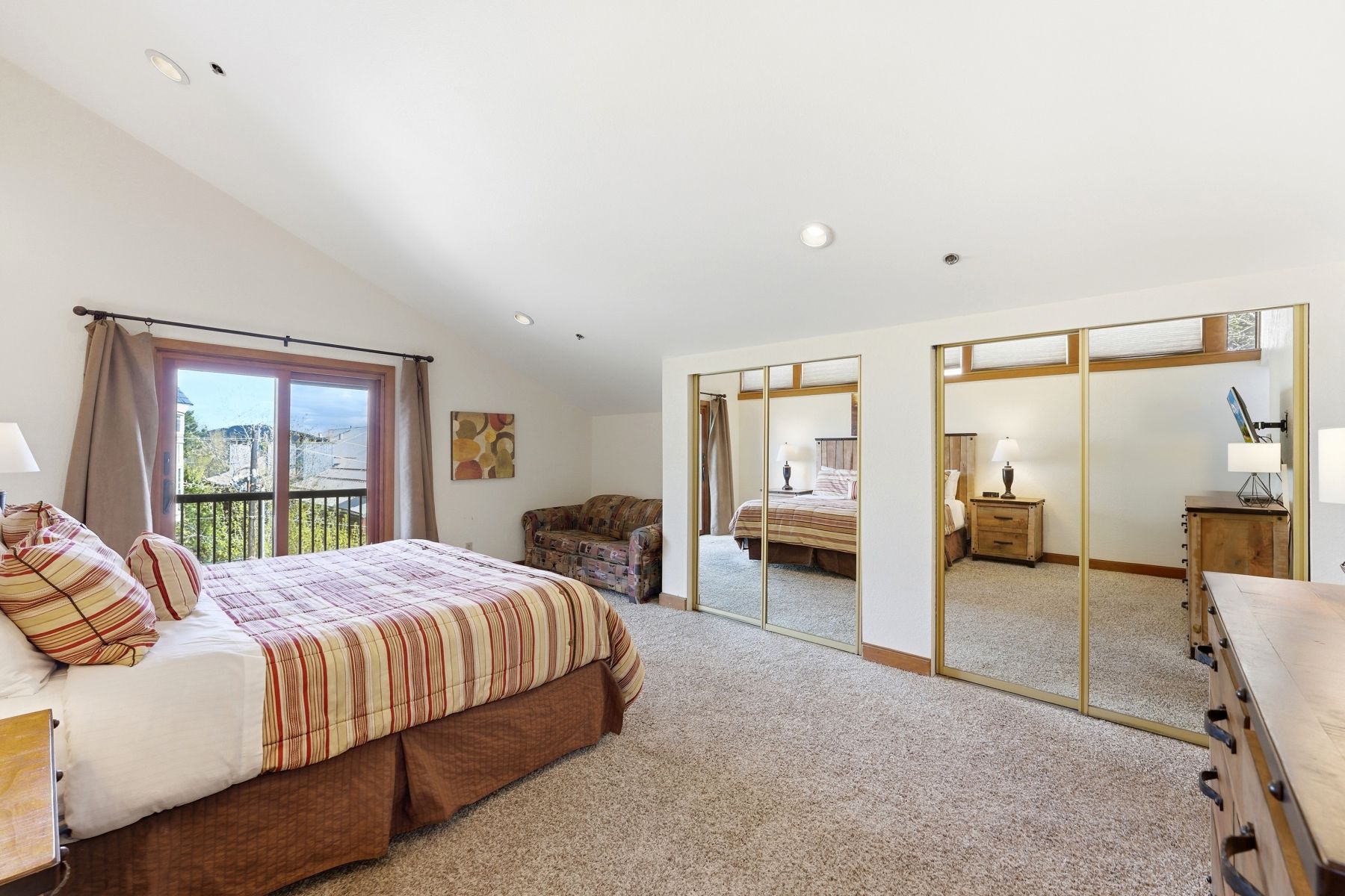 Sloped ceiling bedroom featuring a sliding glass door leading to an outdoor balcony with metal railings, recessed lighting, and mirrored closet doors