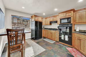 Kitchen featuring wood-finish cabinetry, black appliances, stone-look countertops, and slate flooring
