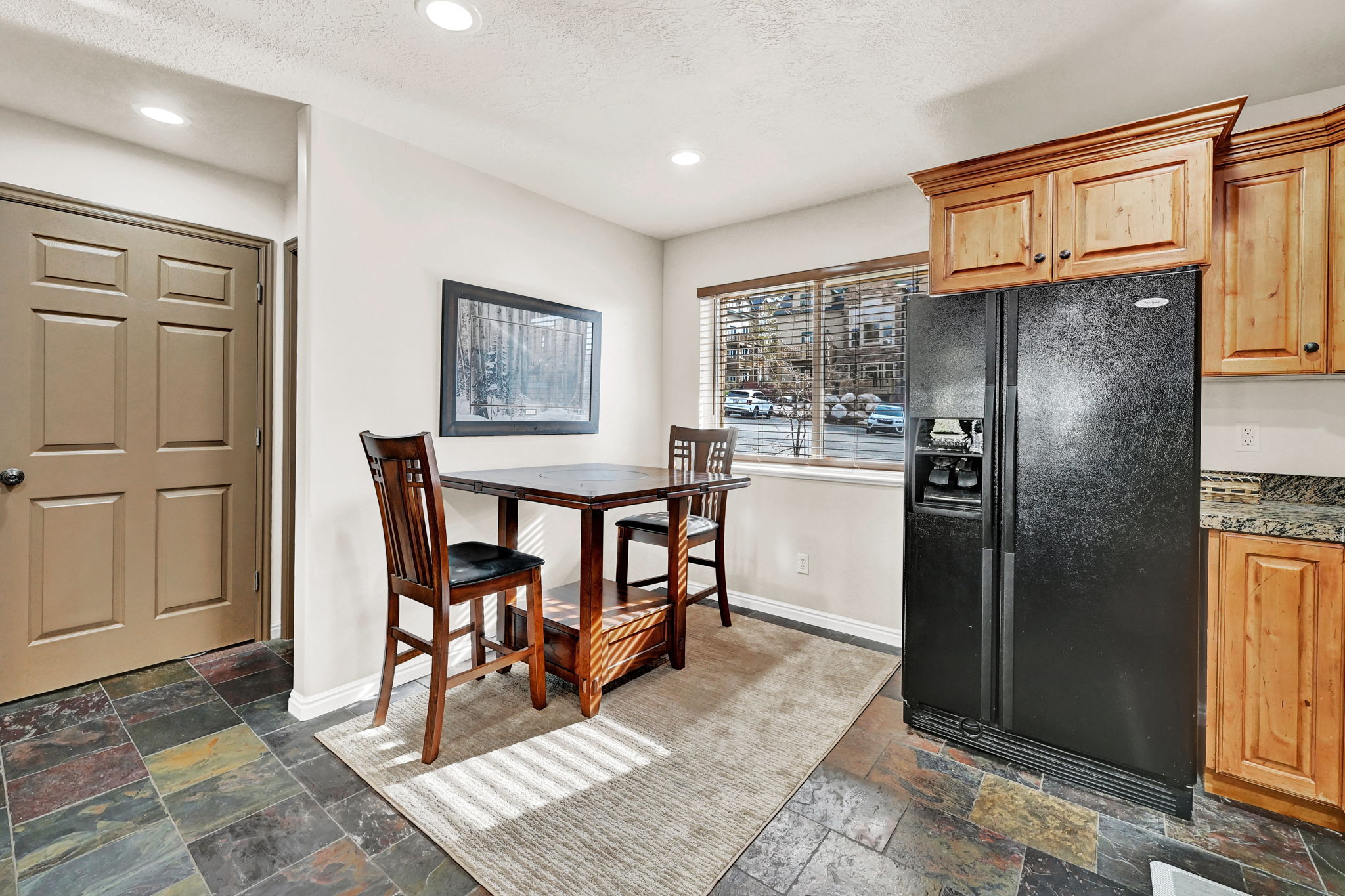 Kitchen area featuring natural wood cabinetry, a black side-by-side refrigerator, and a window with blinds