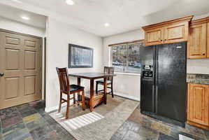 Kitchen area featuring natural wood cabinetry, a black side-by-side refrigerator, and a window with blinds