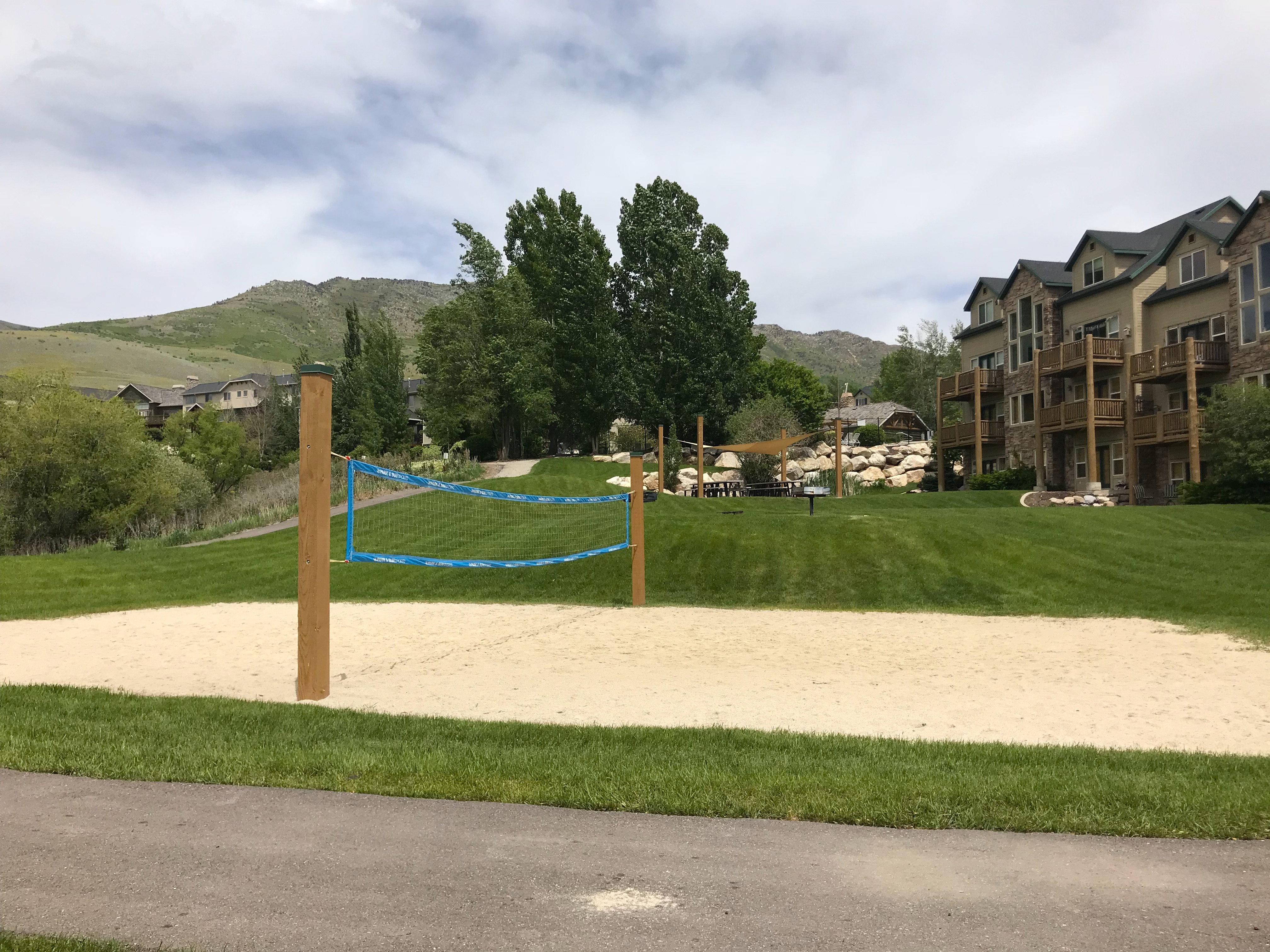 Sand volleyball court with a blue net, surrounded by green lawns