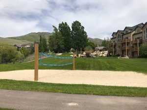 Sand volleyball court with a blue net, surrounded by green lawns