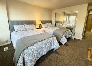 Carpeted room featuring dual beds with upholstered headboards, a mirrored closet, and light-toned walls