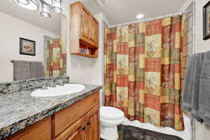 Bathroom featuring a wood-finish vanity with a granite countertop, undermount sink, and a chrome faucet
