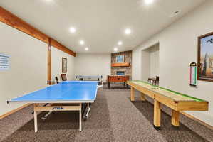 Spacious recreation room featuring recessed lighting, exposed wood beams, and a stone-clad fireplace with a wood mantel