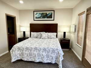 Spacious sleeping area featuring a dark wood headboard, recessed lighting, and textural carpet flooring