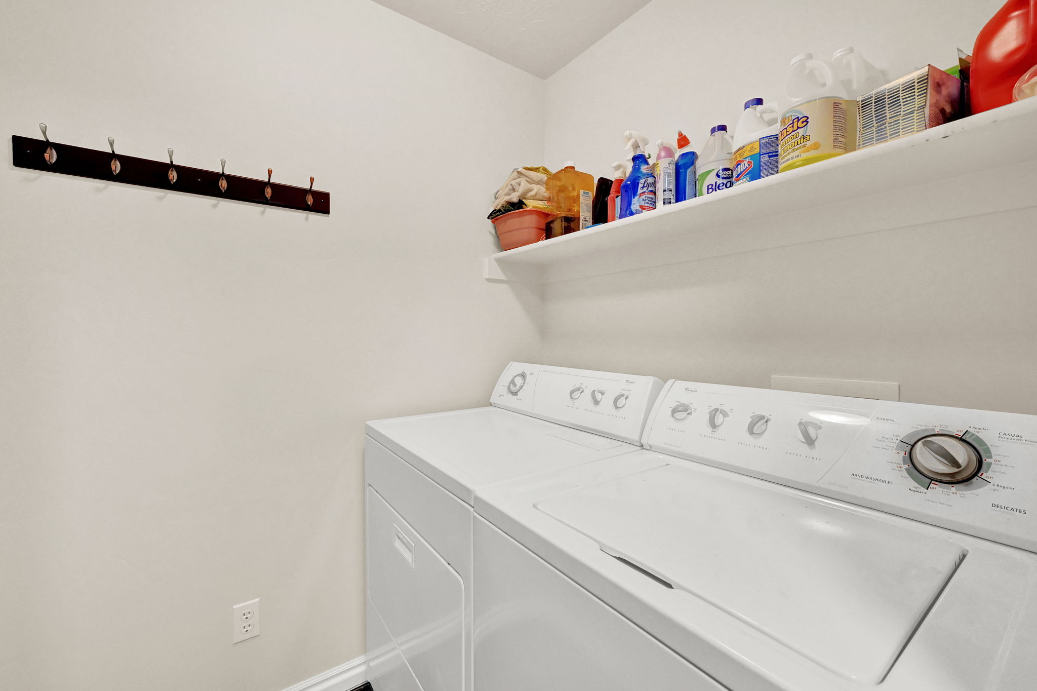 Dedicated laundry area featuring a white top-load washing machine, a white dryer, an upper storage shelf, and a wall-mounted coat rack