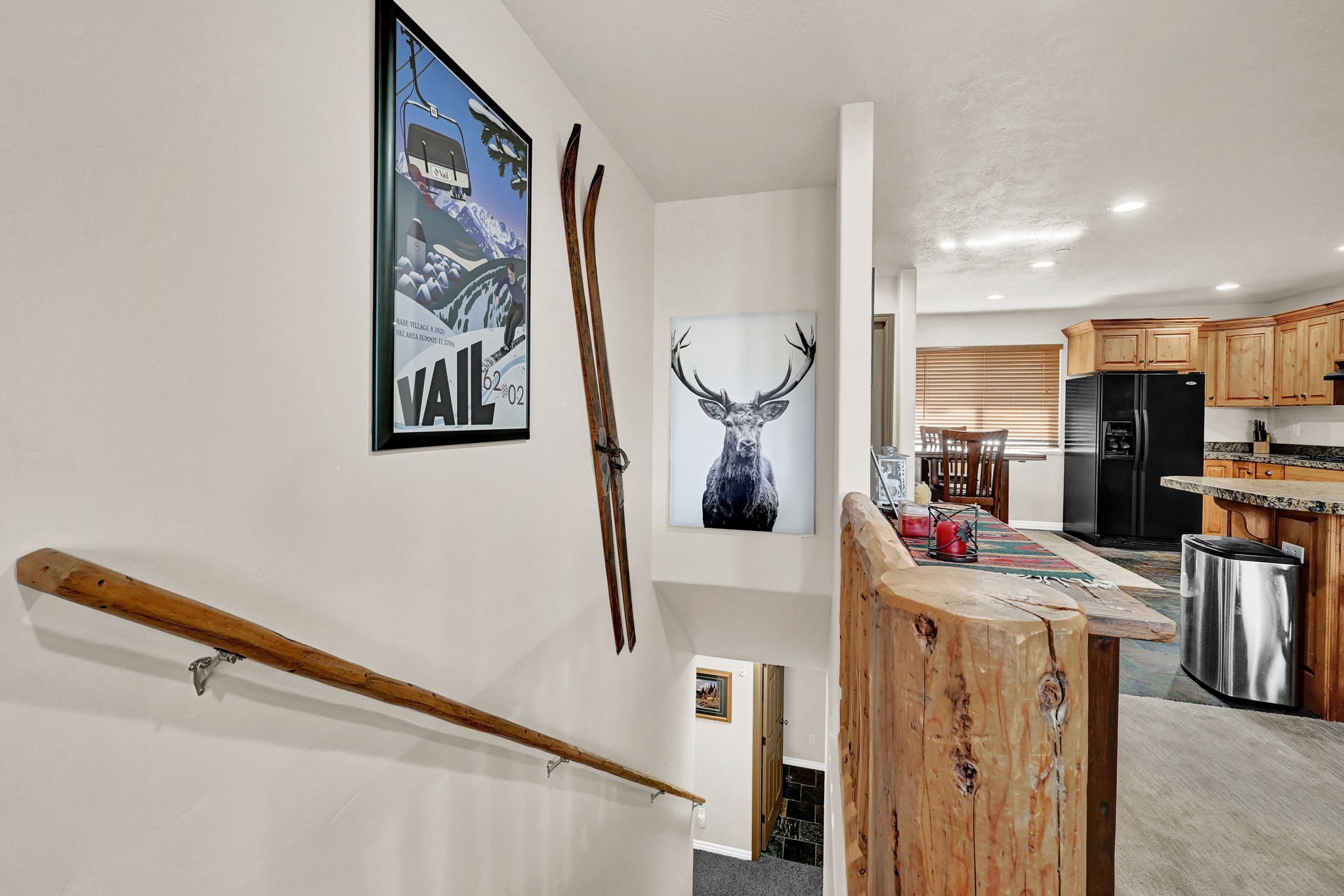 Open-concept living space featuring a rustic wood stair railing, wood-finish flooring, and a kitchen with wood cabinetry, black appliances, and granite-style countertops