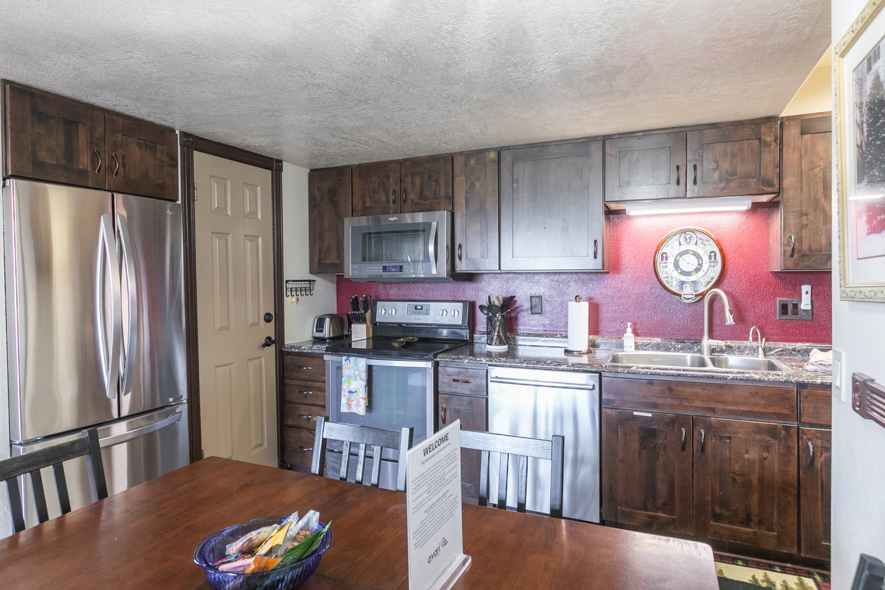 Kitchen featuring stainless steel appliances, wood-finish cabinetry, a dual-basin sink, and a red textured backsplash