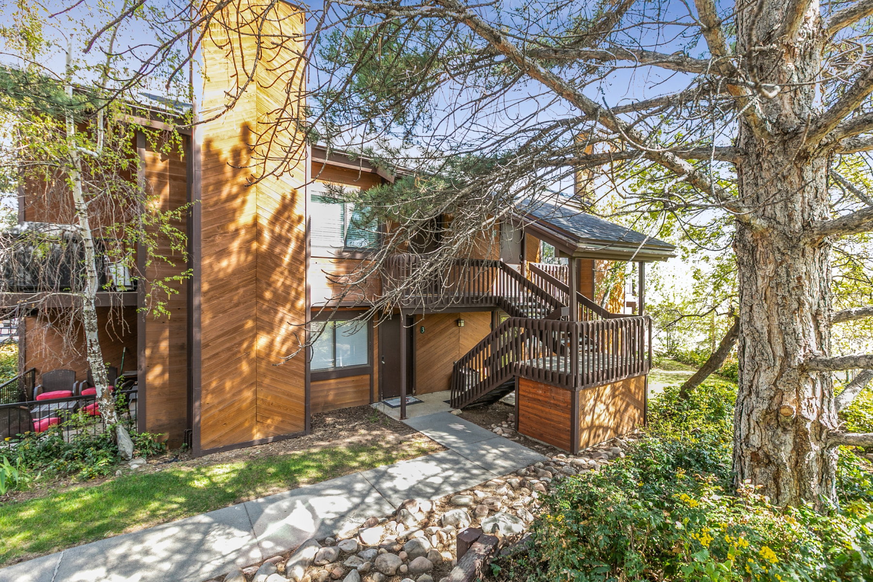 Multi-level property featuring wood-paneled exterior siding, a covered entry porch, and an exterior staircase with dark wood railings