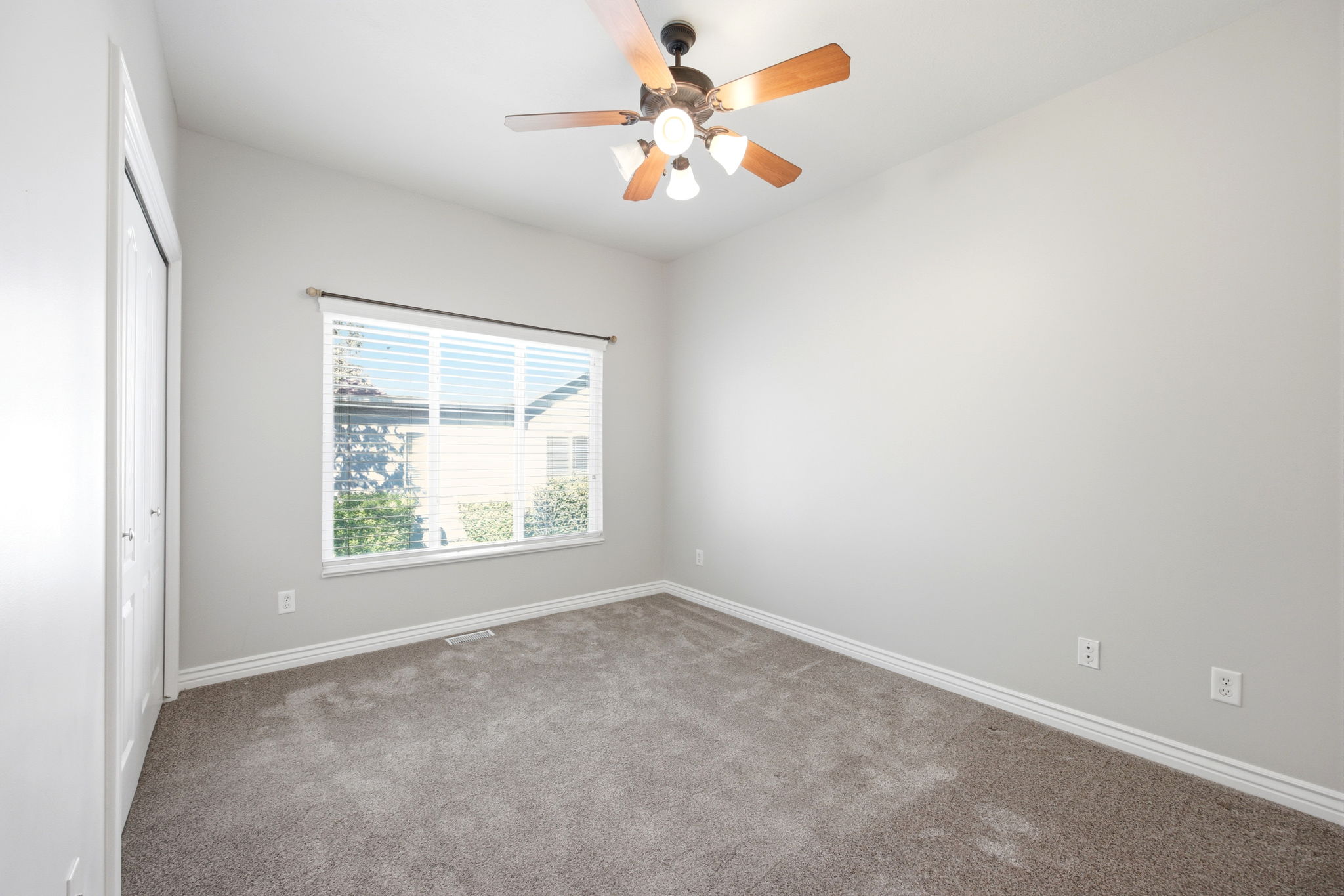 Carpeted room featuring a ceiling fan with light fixture, a window with horizontal blinds, and bi-fold closet doors