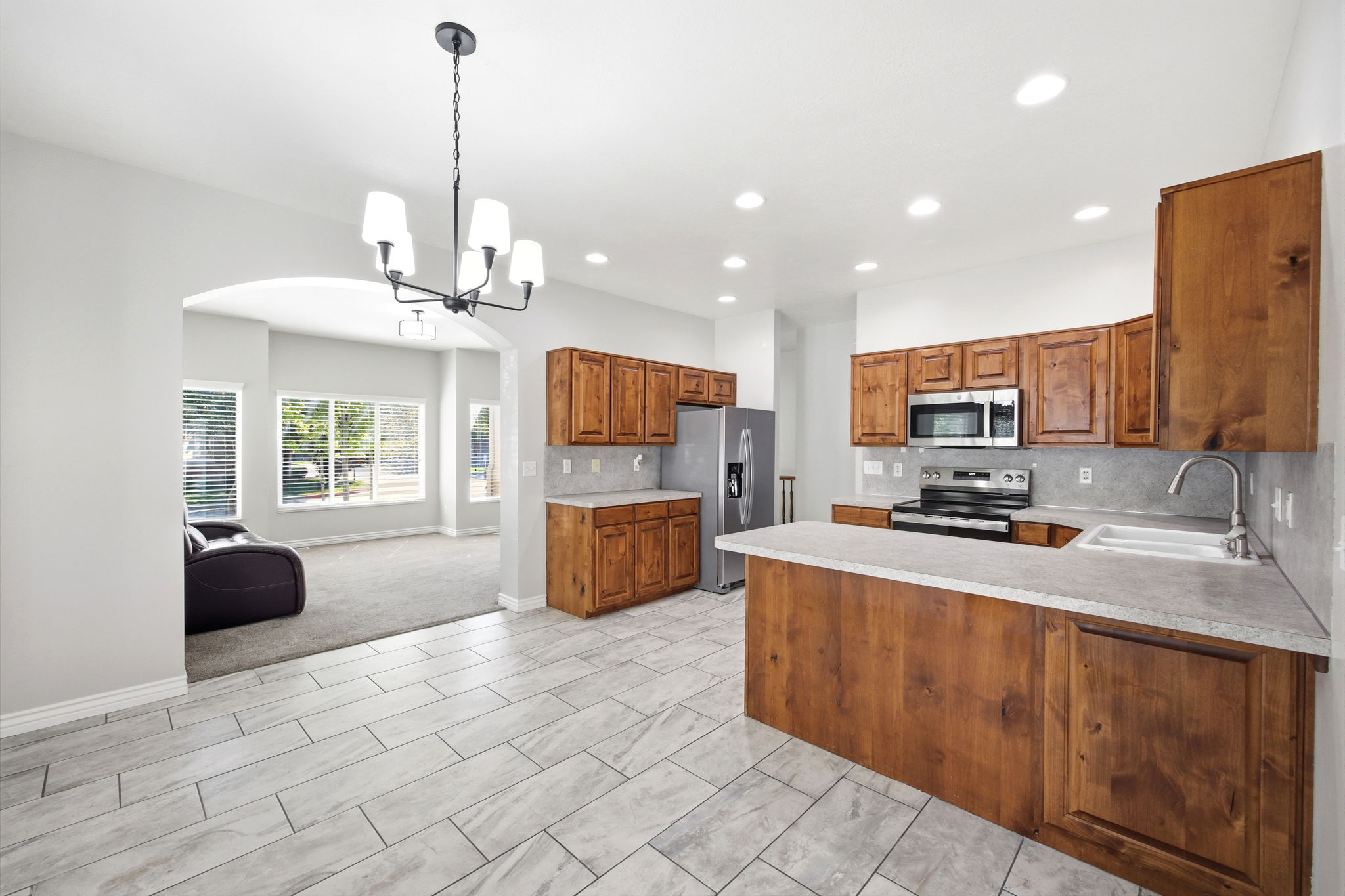 Kitchen featuring wood cabinetry, stainless steel appliances, a white sink, light-toned countertops, and light gray rectangular tile flooring