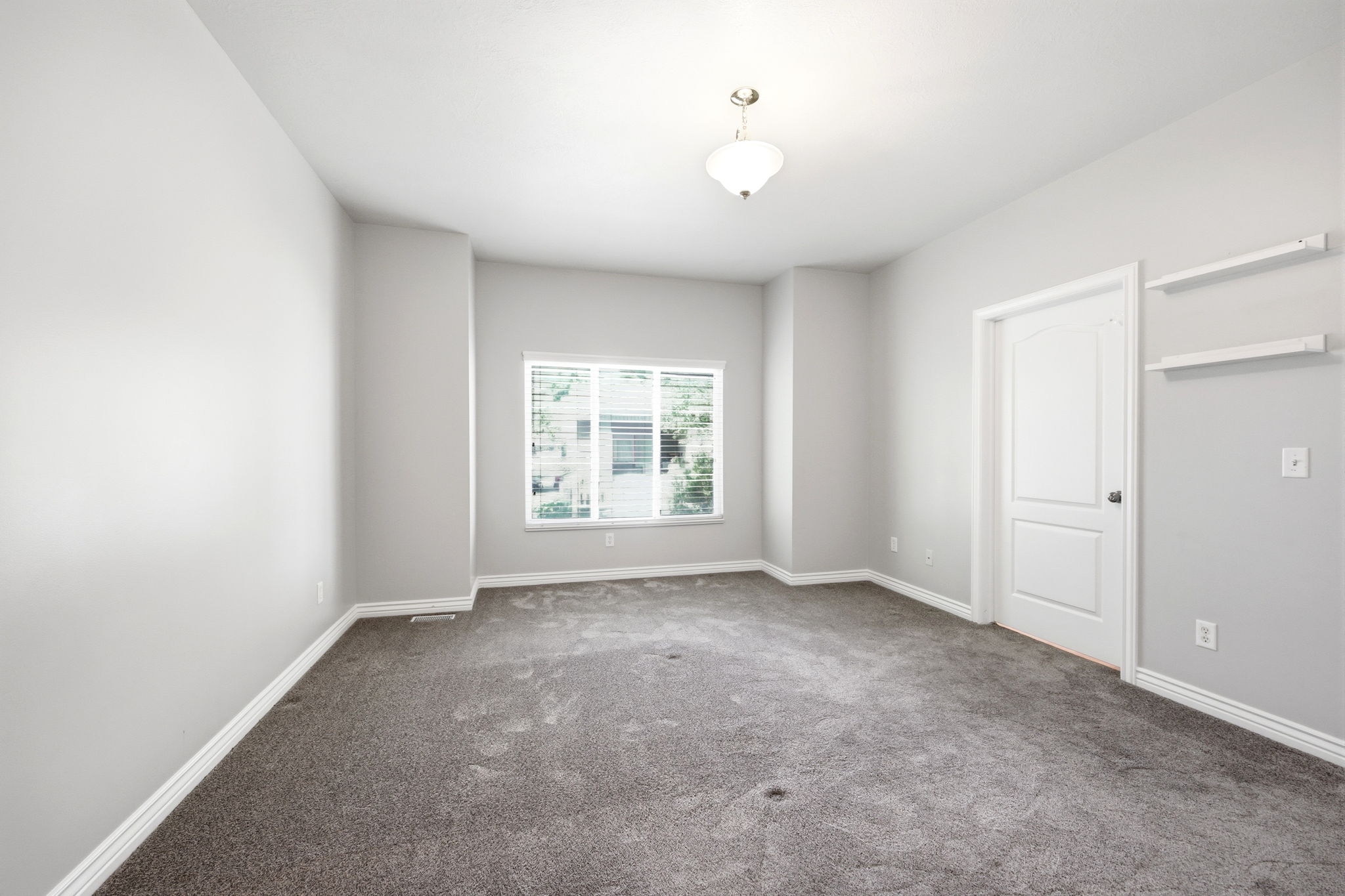 Spacious interior room featuring light gray walls, plush gray carpeting, and white baseboards