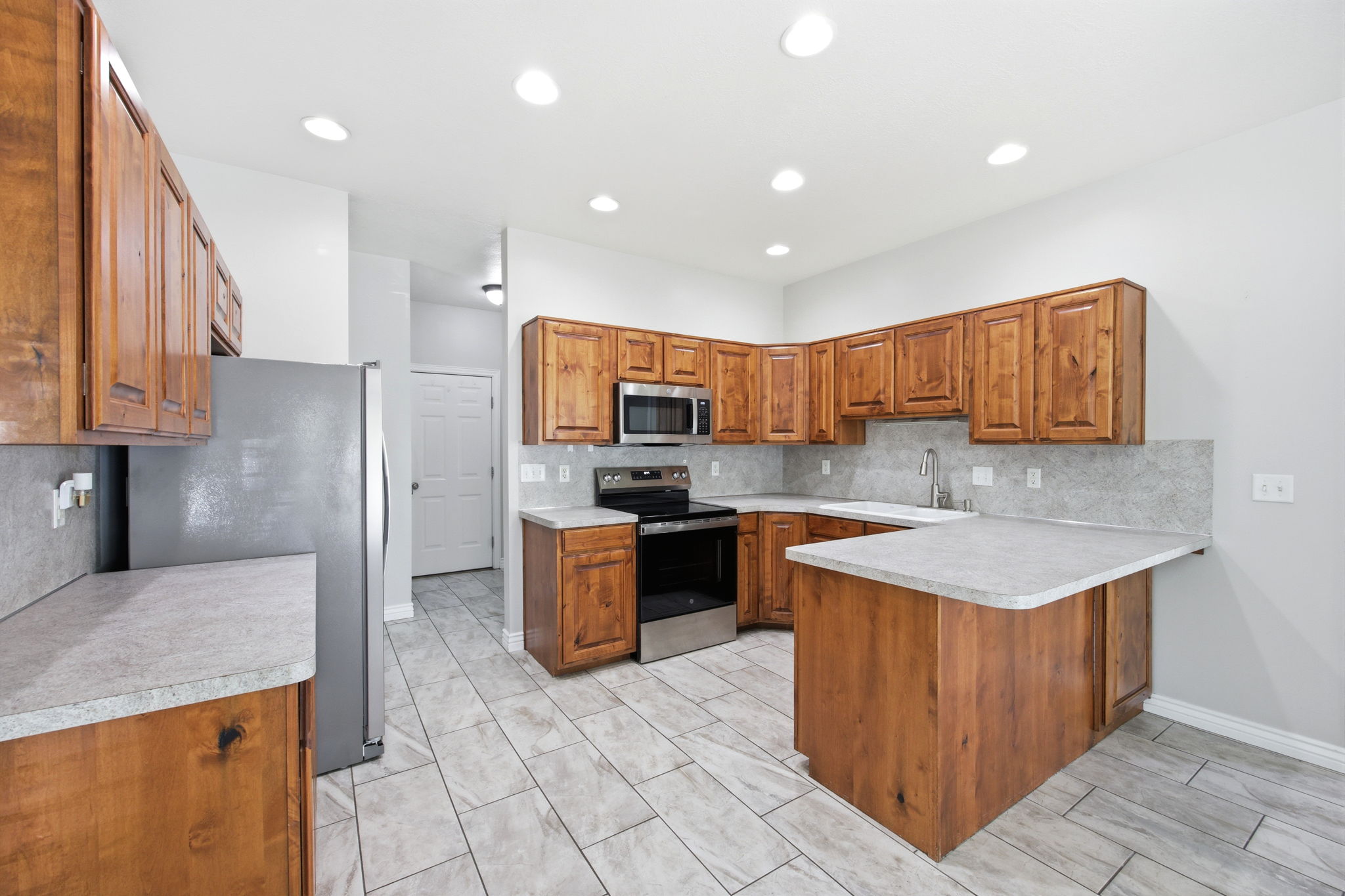 Kitchen featuring wood cabinetry, stainless steel appliances, light-toned countertops, tile backsplash, and recessed lighting
