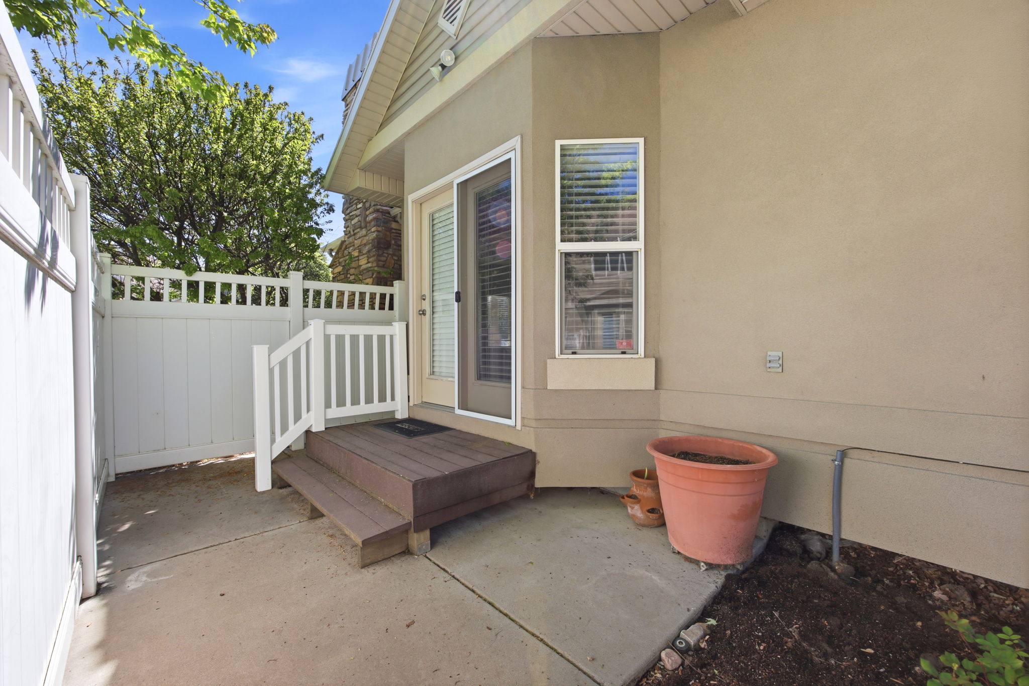 Private patio area featuring a sliding glass door, composite steps with white railings, concrete paving, and a white privacy fence