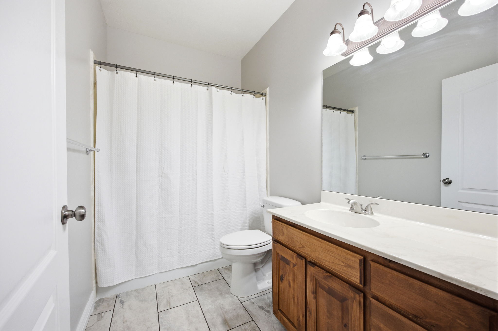 Bathroom featuring a wood-finish vanity with a single basin sink and light-colored countertop