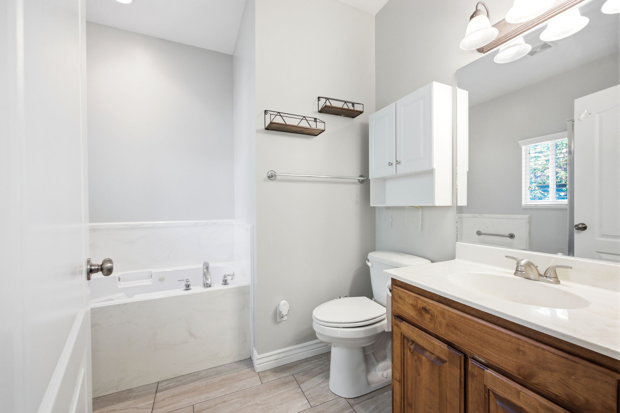 Bathroom featuring a built-in tub with chrome fixtures, a wood-finish vanity with a white countertop and integrated sink, a wall-mounted medicine cabinet, and light-toned tile flooring