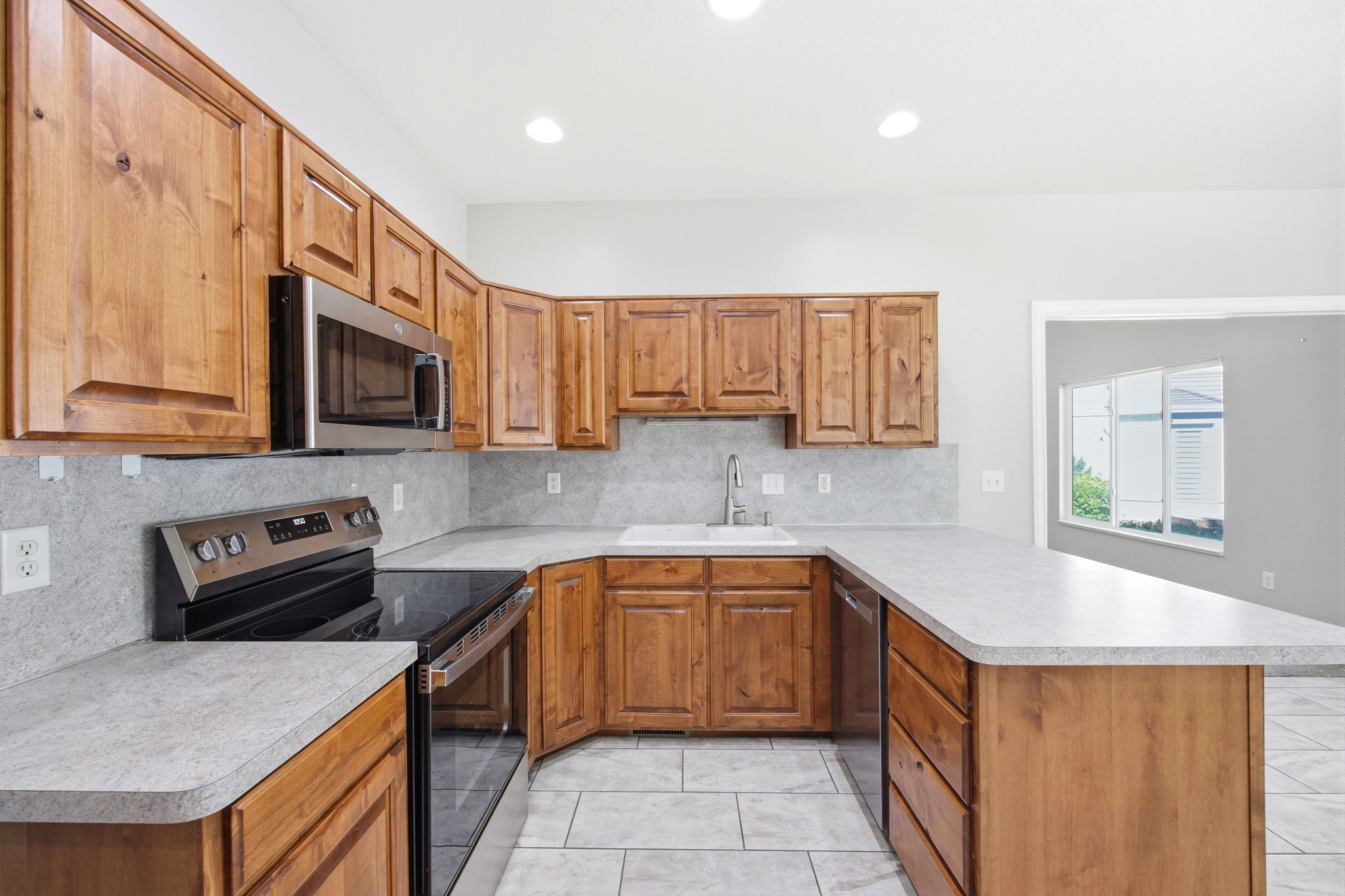 Kitchen featuring wood cabinetry, stainless steel appliances, a composite sink with a gooseneck faucet, light-toned countertops, and tile flooring