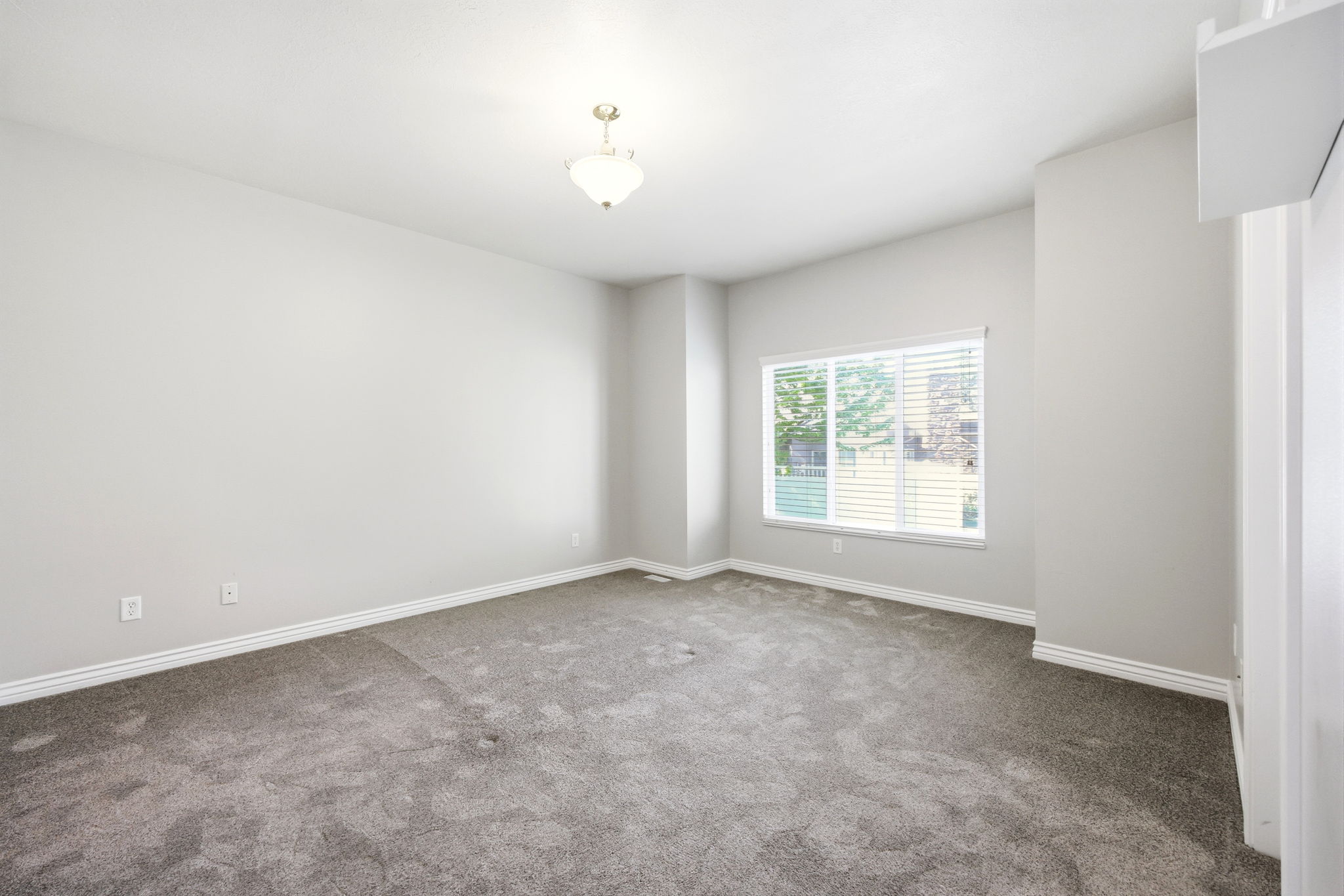 Carpeted room featuring a single window with blinds, a ceiling-mounted light fixture, and white baseboards
