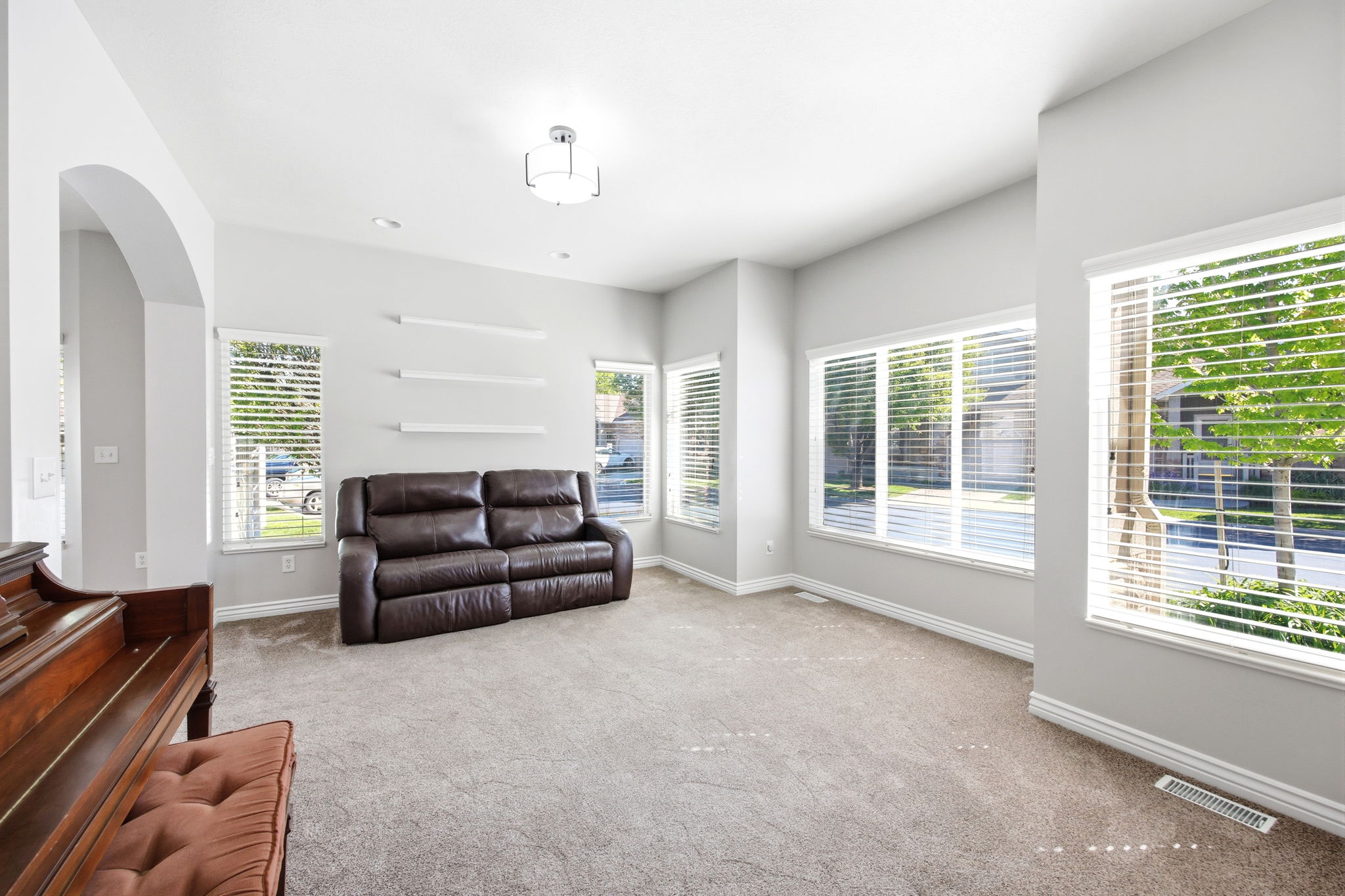 Spacious carpeted room featuring multiple large windows with horizontal blinds, an arched doorway, built-in wall shelving, and a semi-flush mount ceiling light fixture