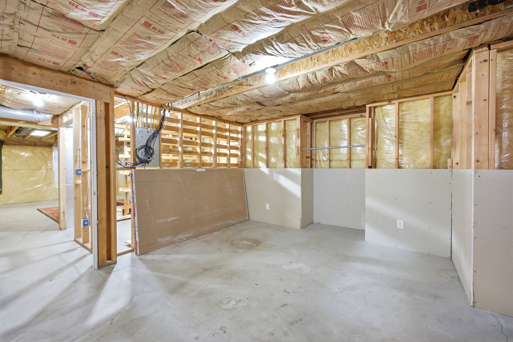Unfinished basement featuring exposed wood framing, concrete flooring, and partial drywall installation