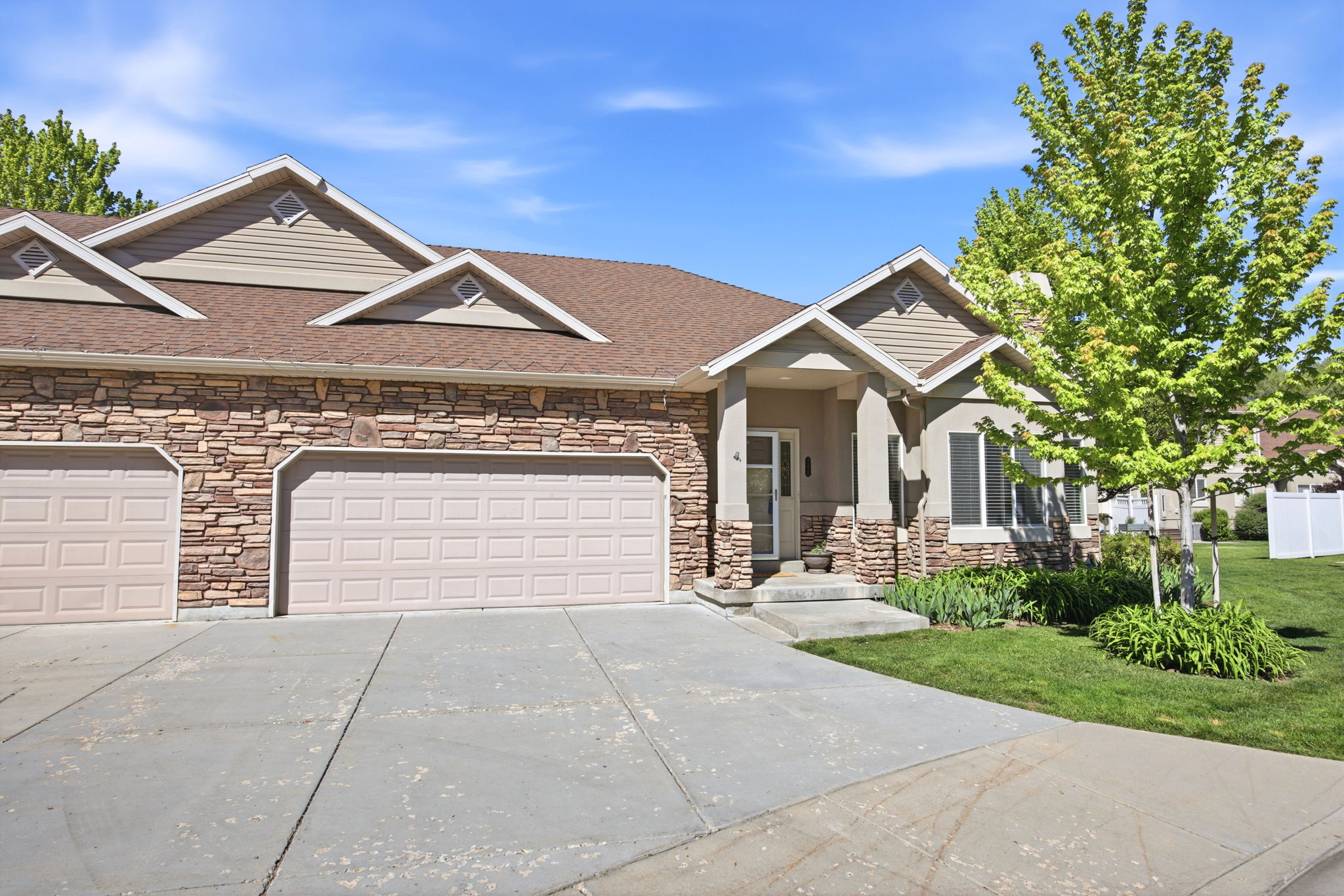 Stone veneer exterior featuring multiple garage bays, a covered entry, and a manicured lawn