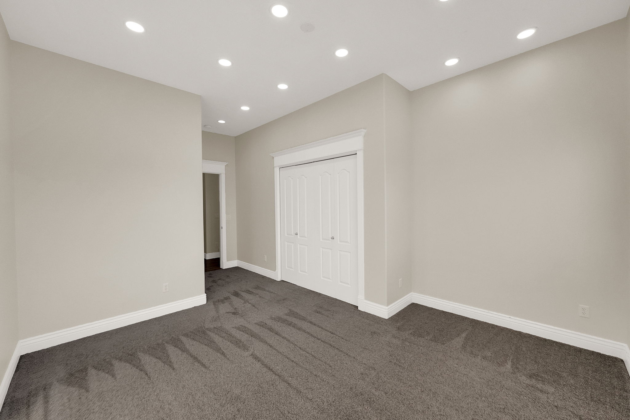 Spacious room featuring neutral-toned walls, recessed lighting, and dark grey carpeting