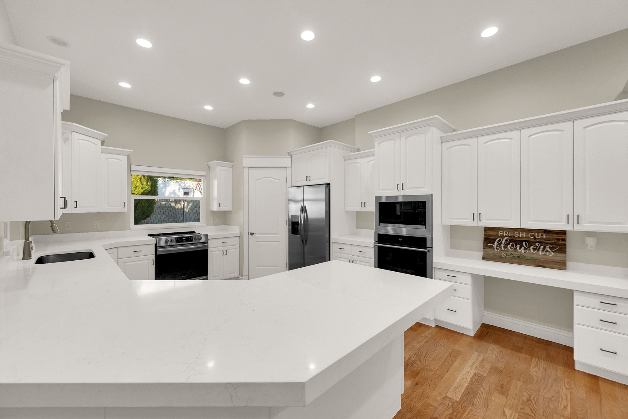 Spacious kitchen featuring white cabinetry, light countertops, wood-finish flooring, recessed lighting, and stainless steel appliances