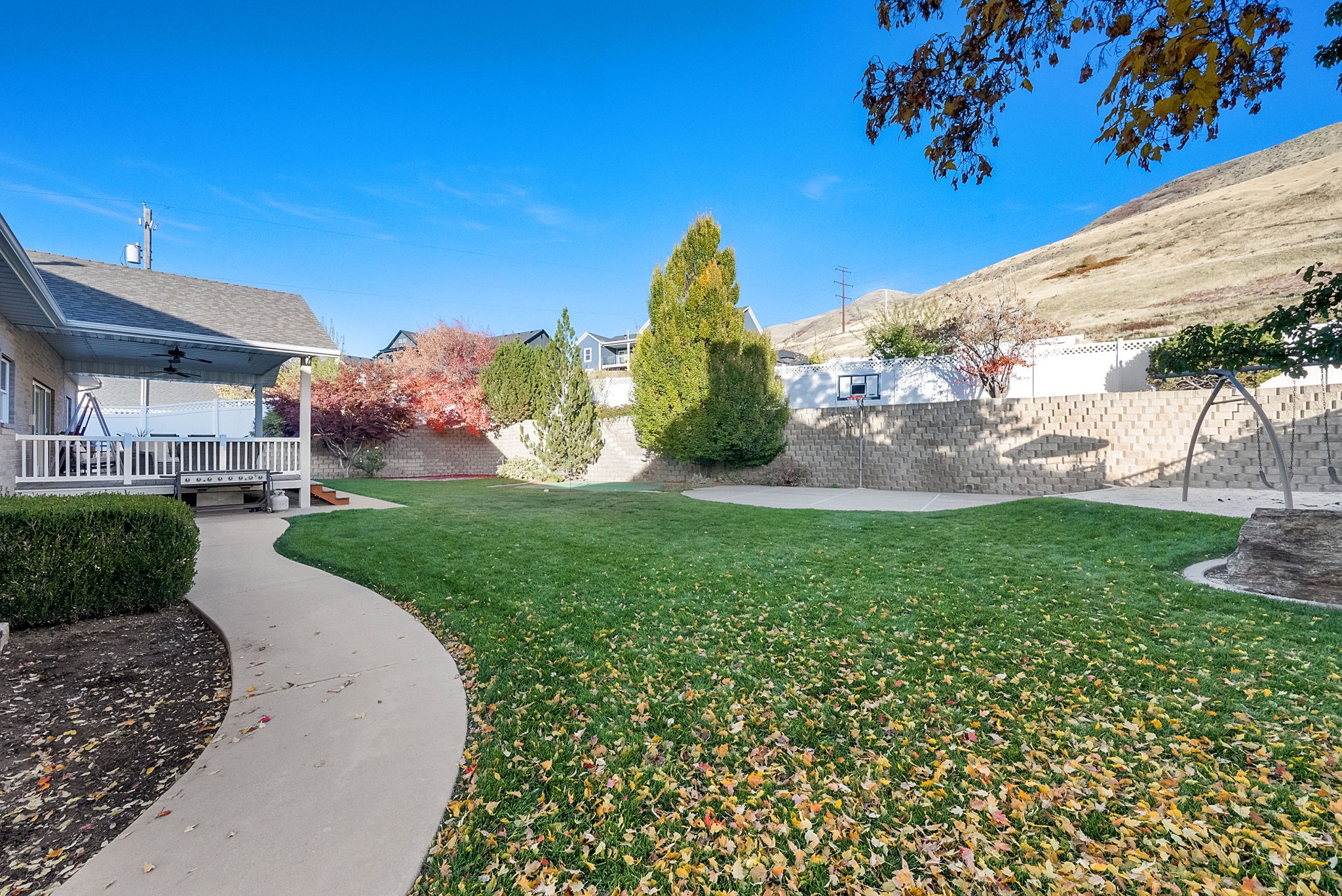 Spacious backyard featuring a manicured lawn, curved concrete pathway, and a covered patio with white railing