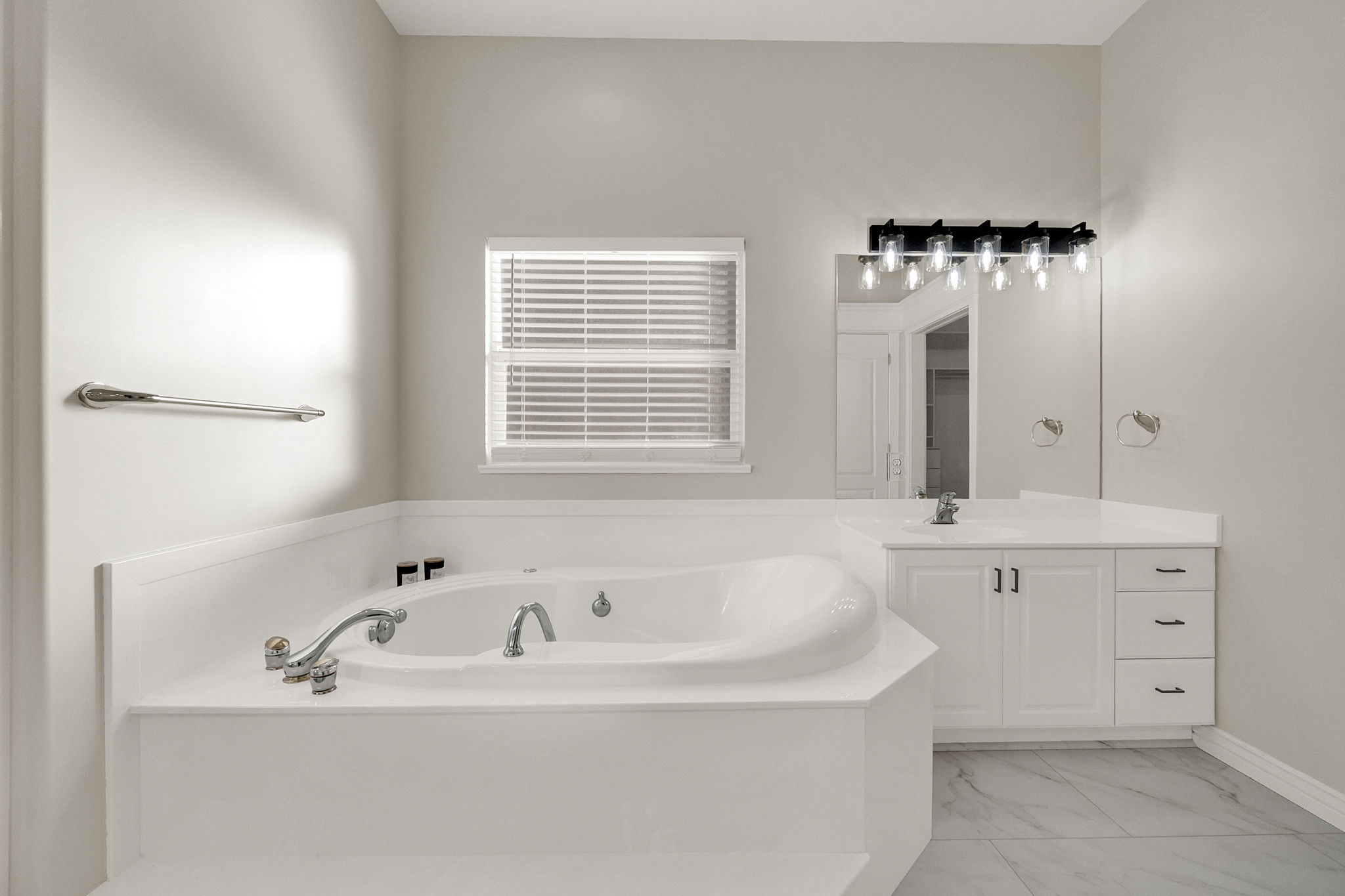 Built-in soaking tub with chrome fixtures, white vanity with integrated sink, quartz-finish countertop, and black vanity lighting