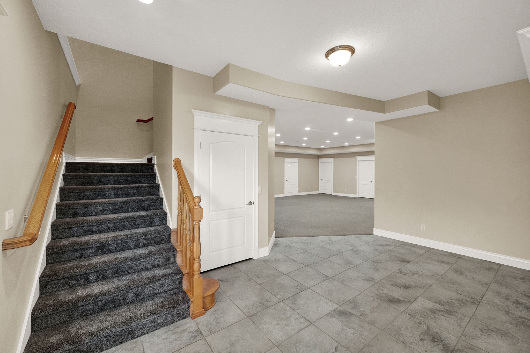 Carpeted staircase with wood handrails, opening to a tiled entry area