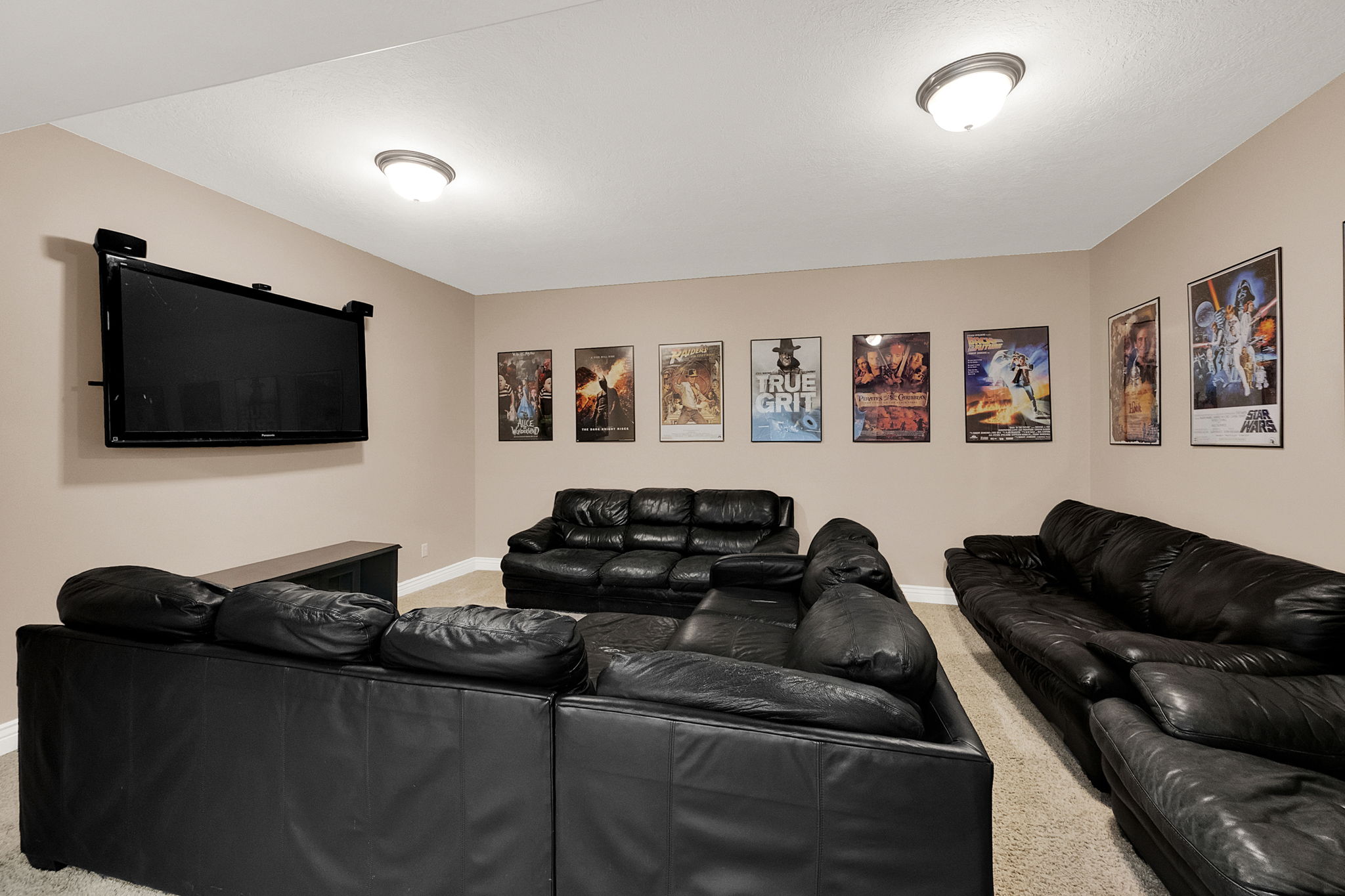 Spacious media room featuring wall-mounted television, recessed ceiling lights, and light-toned wall paint