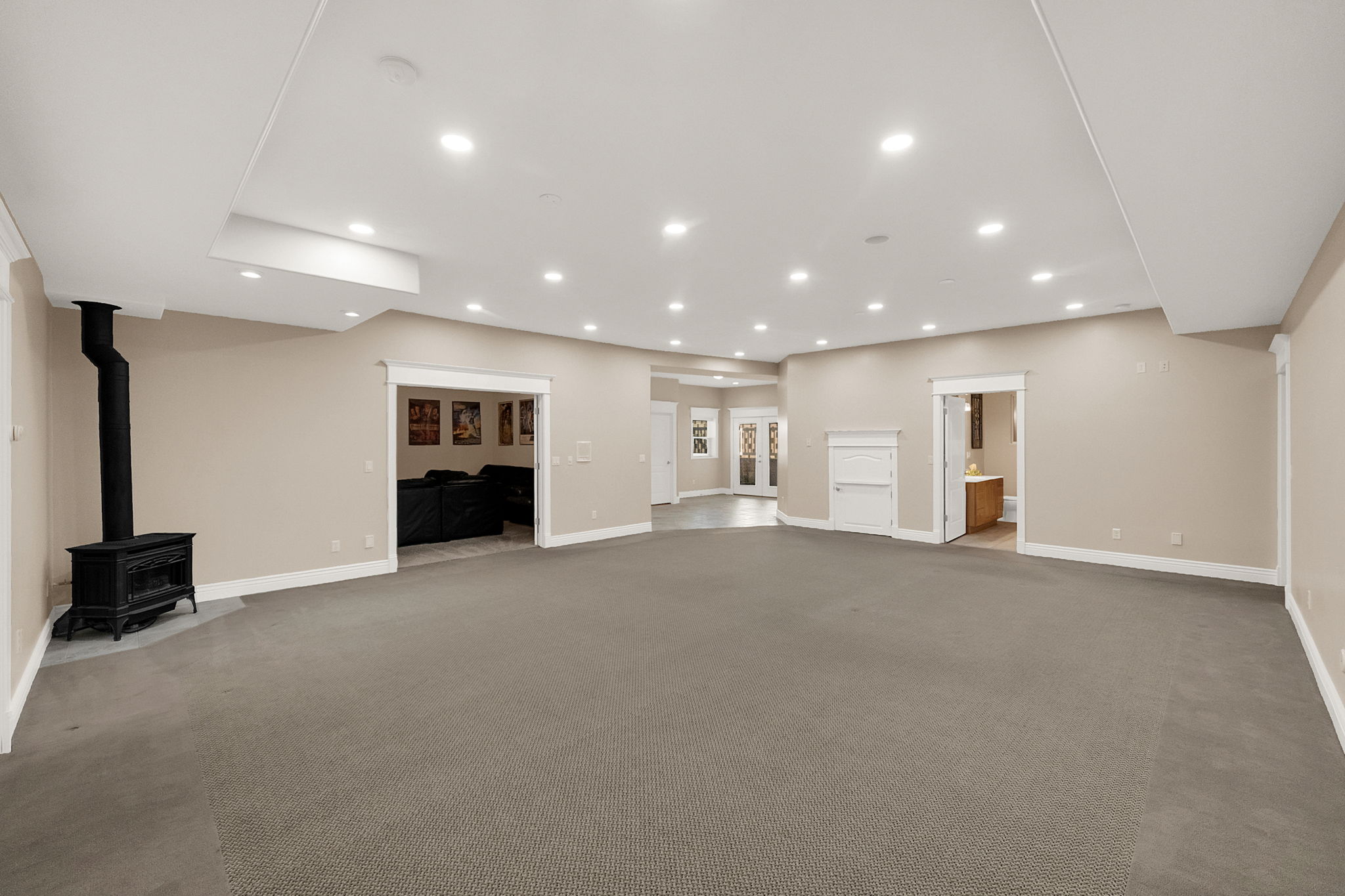 Expansive carpeted room featuring a freestanding black stove, recessed lighting, and multiple distinct entryways