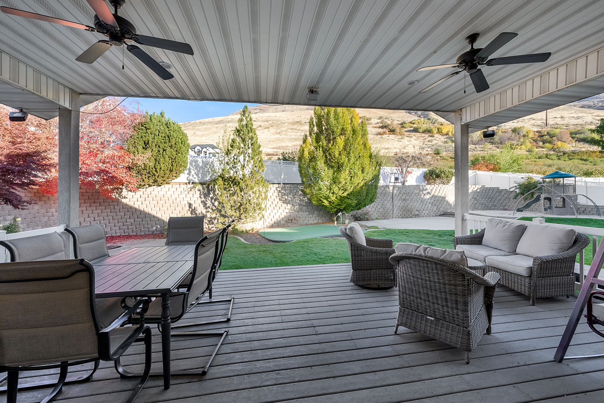Covered outdoor deck with ceiling fans, composite decking, and direct access to a putting green and terraced backyard with a block retaining wall