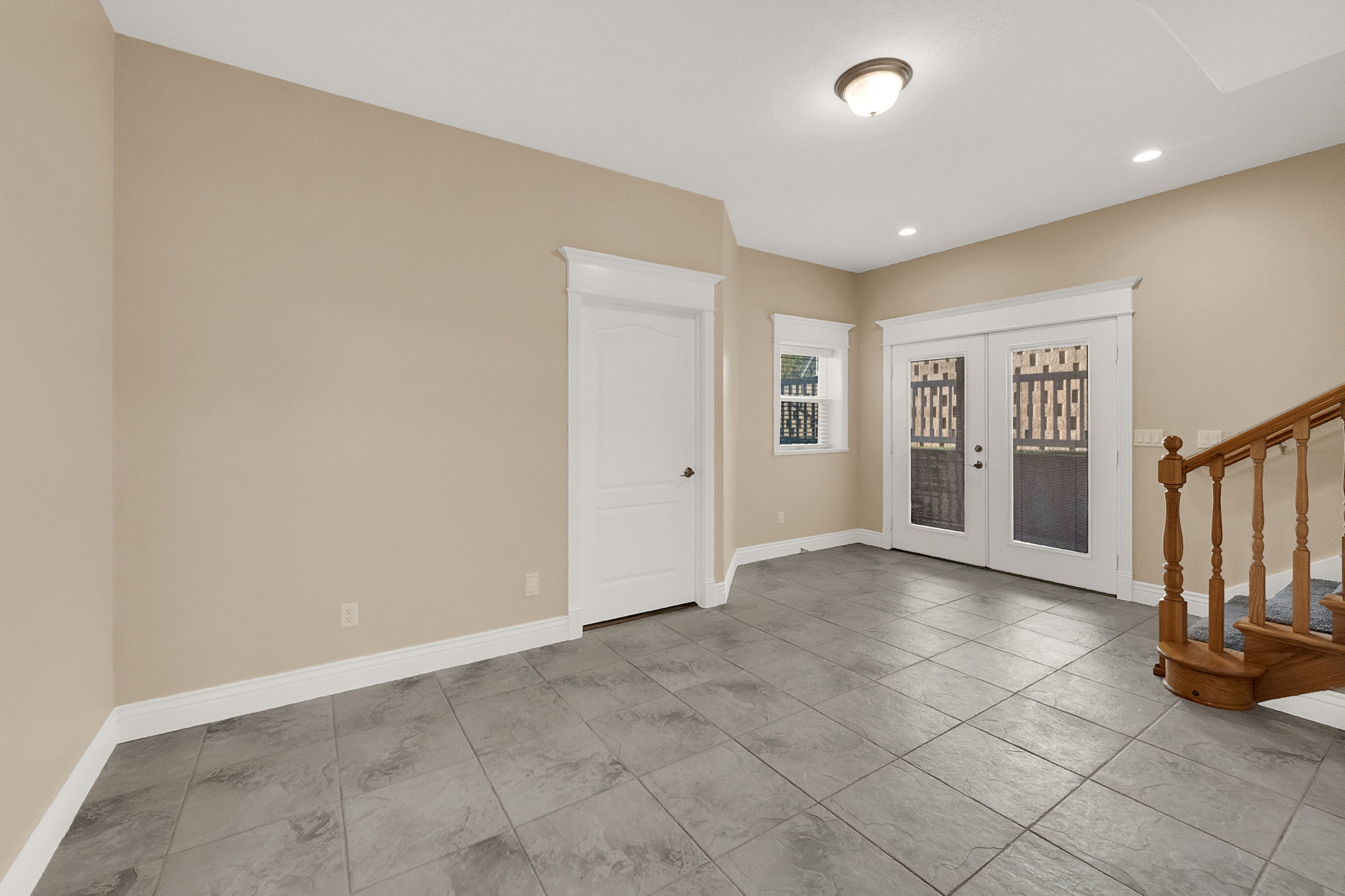 Spacious room featuring gray tile flooring, a white paneled door, and French doors with decorative glass panels