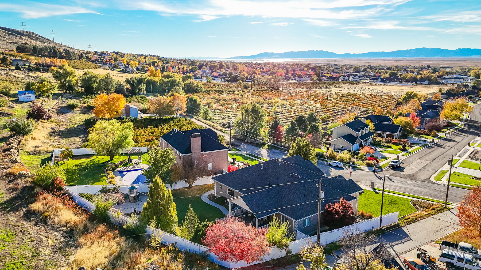 Aerial perspective showcasing a residential property with a dark shingle roof, a surrounding white fence, and mature trees