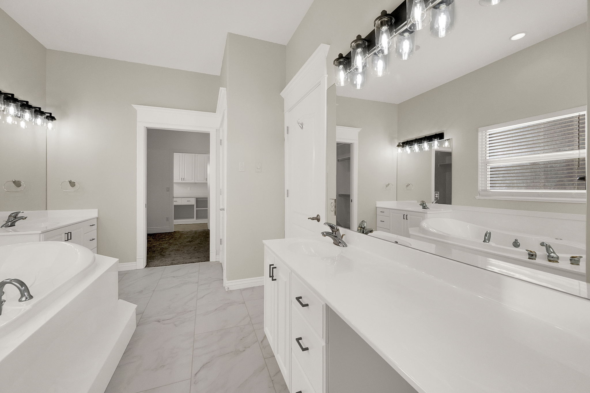 Spacious bathroom featuring a built-in soaking tub, dual vanity with white cabinetry, large vanity mirrors, and contemporary light fixtures