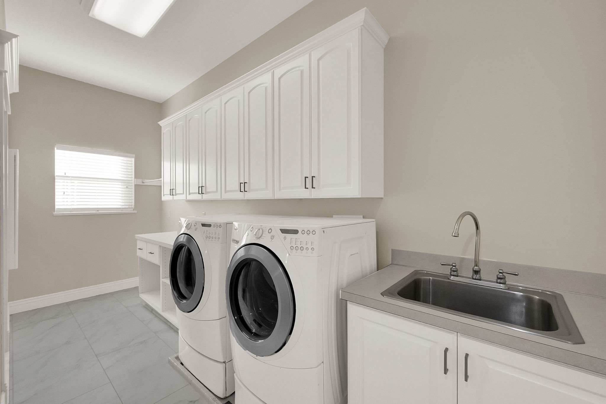 Dedicated laundry room featuring extensive white cabinetry, a built-in utility sink, a spacious countertop, and tile flooring
