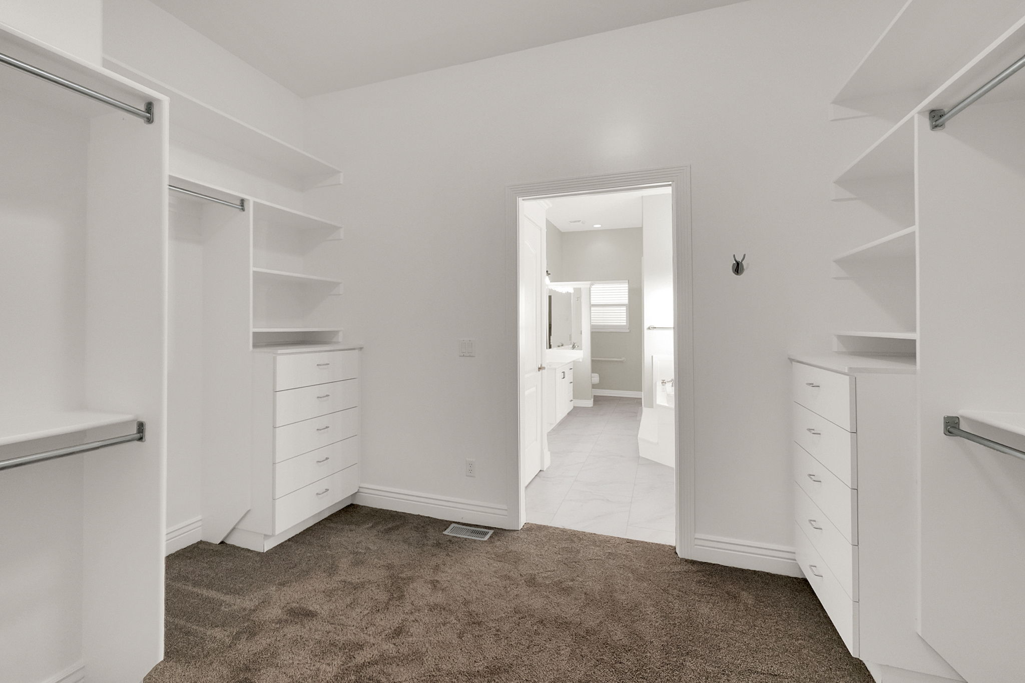 Walk-in closet with built-in white shelving, integrated drawers, and chrome hanging rods