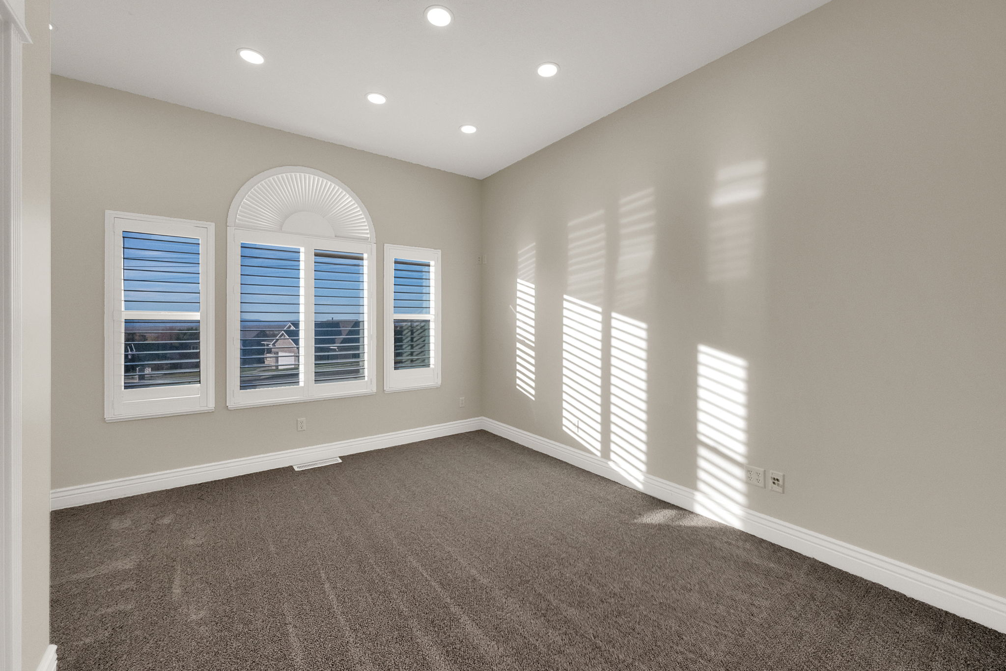 Spacious room featuring multiple windows with integrated plantation shutters, recessed lighting, neutral wall tones, and carpet flooring