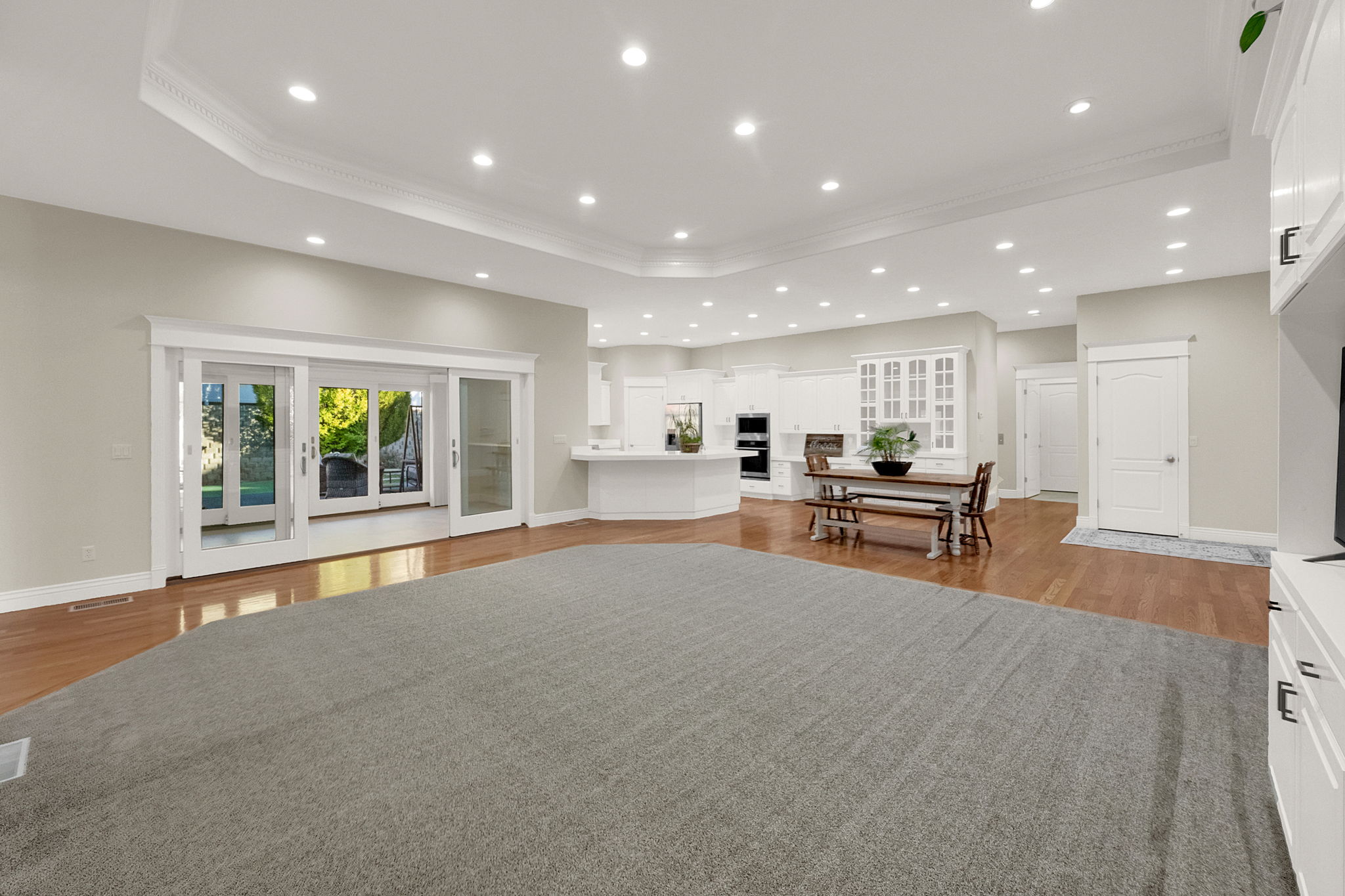 Recessed lighting illuminates an expansive room featuring a tray ceiling with crown molding, hardwood flooring, and sliding glass doors