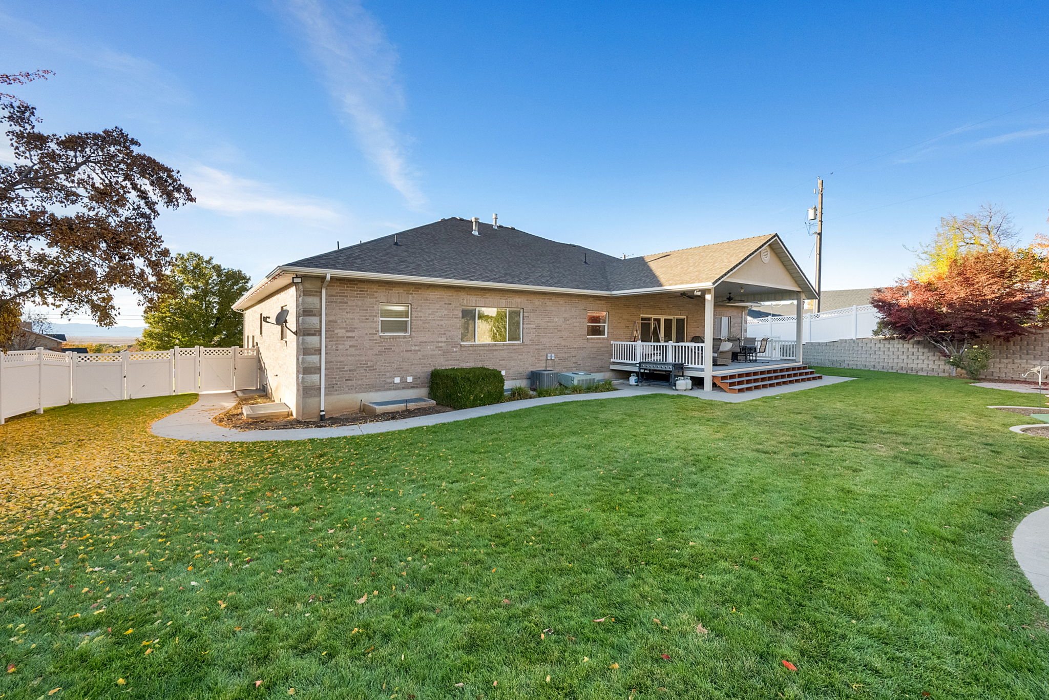 Expansive backyard featuring a manicured lawn, a paved patio, and a multi-level deck with a covered portion