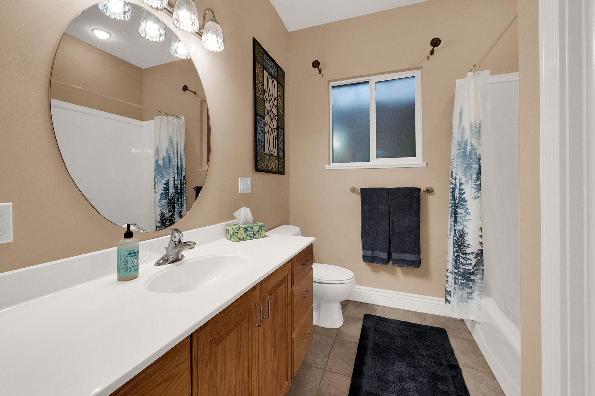 Bathroom featuring a spacious vanity with integrated sink, wood-finish cabinetry, and a large oval mirror