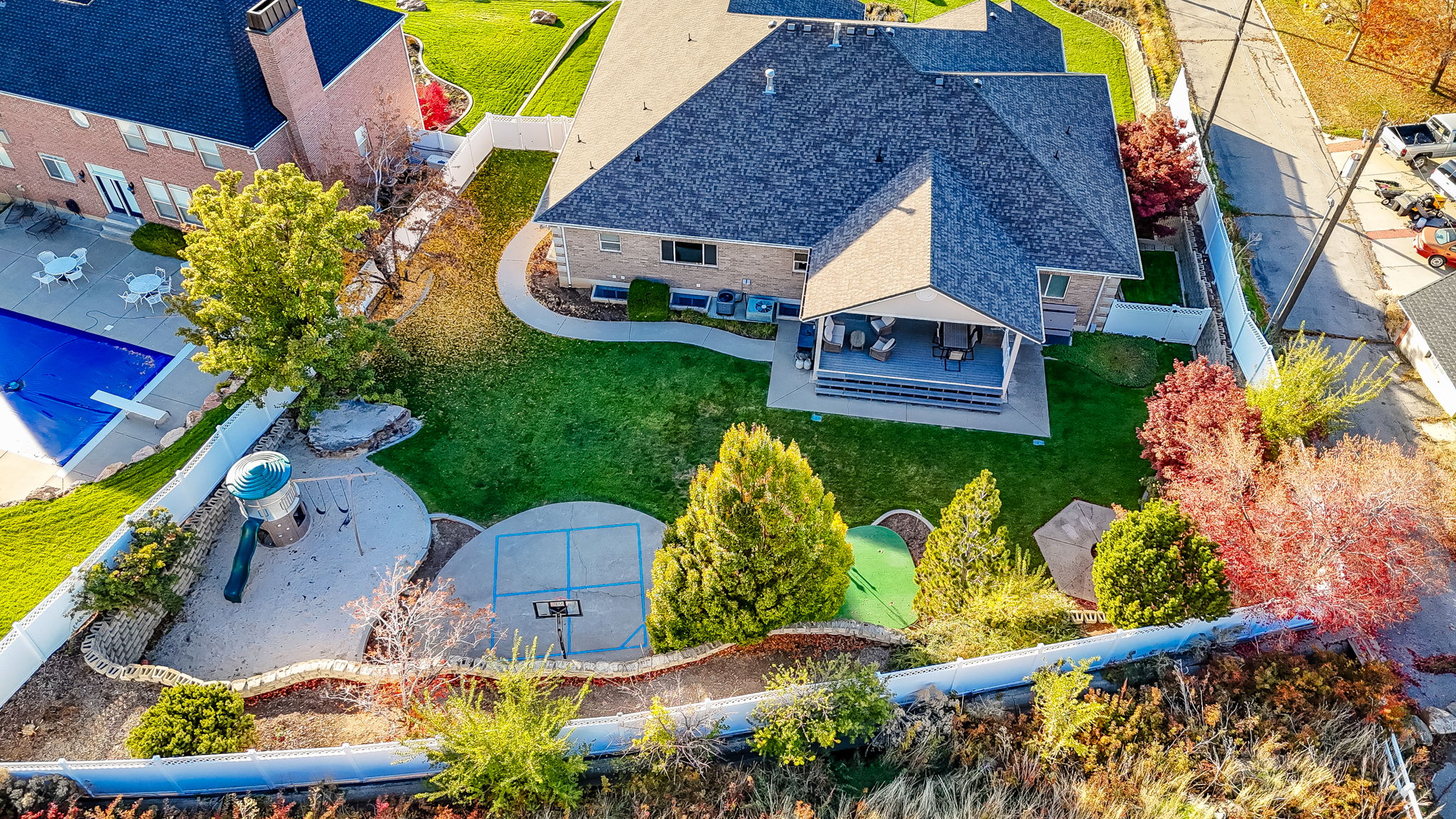 Spacious backyard featuring a covered patio, expansive lawn, playground area, and a dedicated sport court