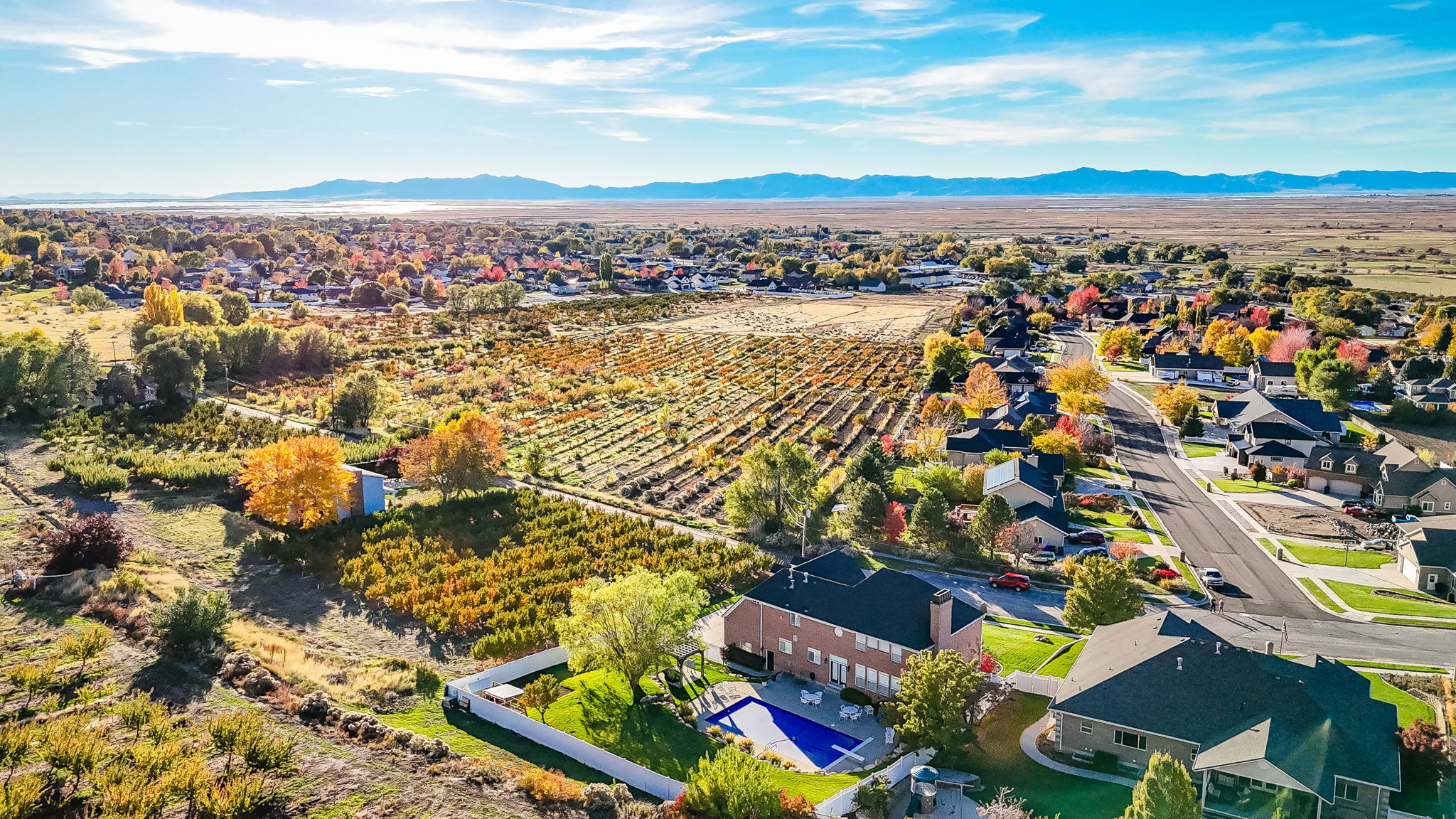 Expansive aerial perspective showcasing a residential neighborhood with varied home styles, bordered by agricultural fields